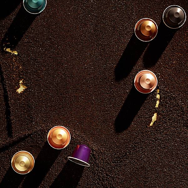 Capsule di caffè in diversi colori poggiano su una superficie scura con ombre.