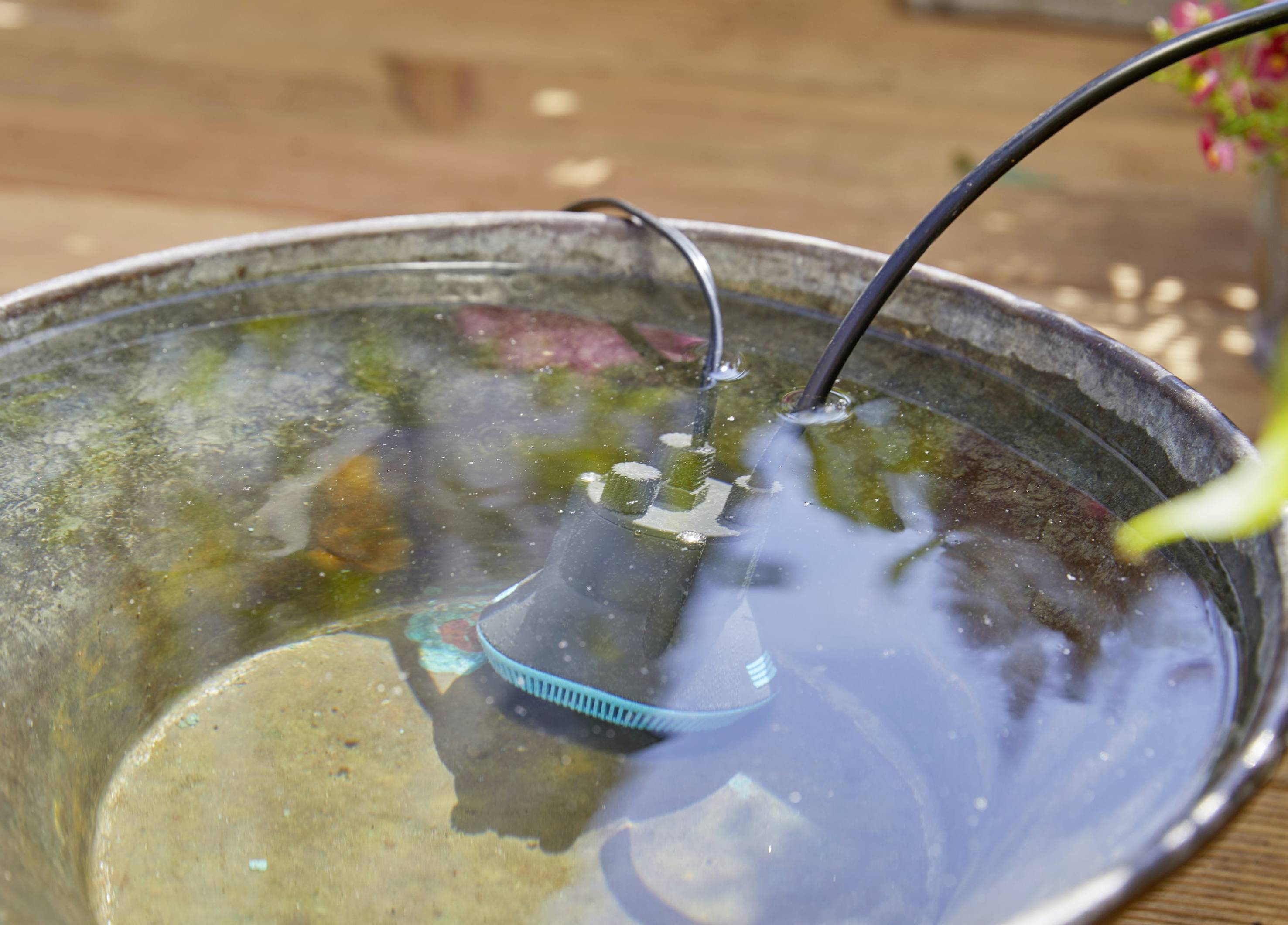 Un dispositivo elettrico nero galleggia parzialmente in una ciotola metallica riempita d'acqua. Un cavo fuoriesce dal dispositivo.