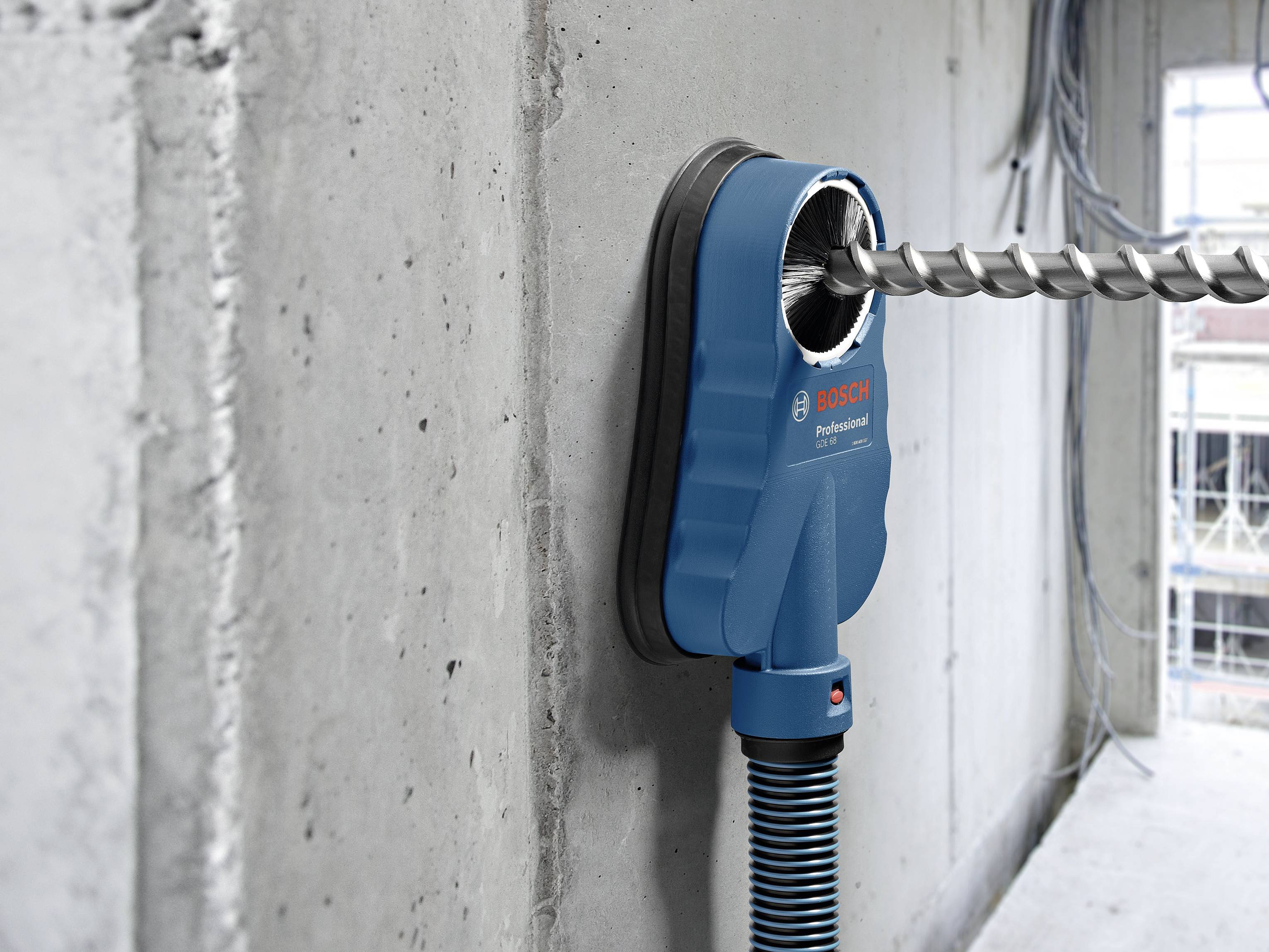 Trapano con aspirapolvere perfora un foro in un muro di cemento. La polvere viene aspirata direttamente dall'apposito accessorio.