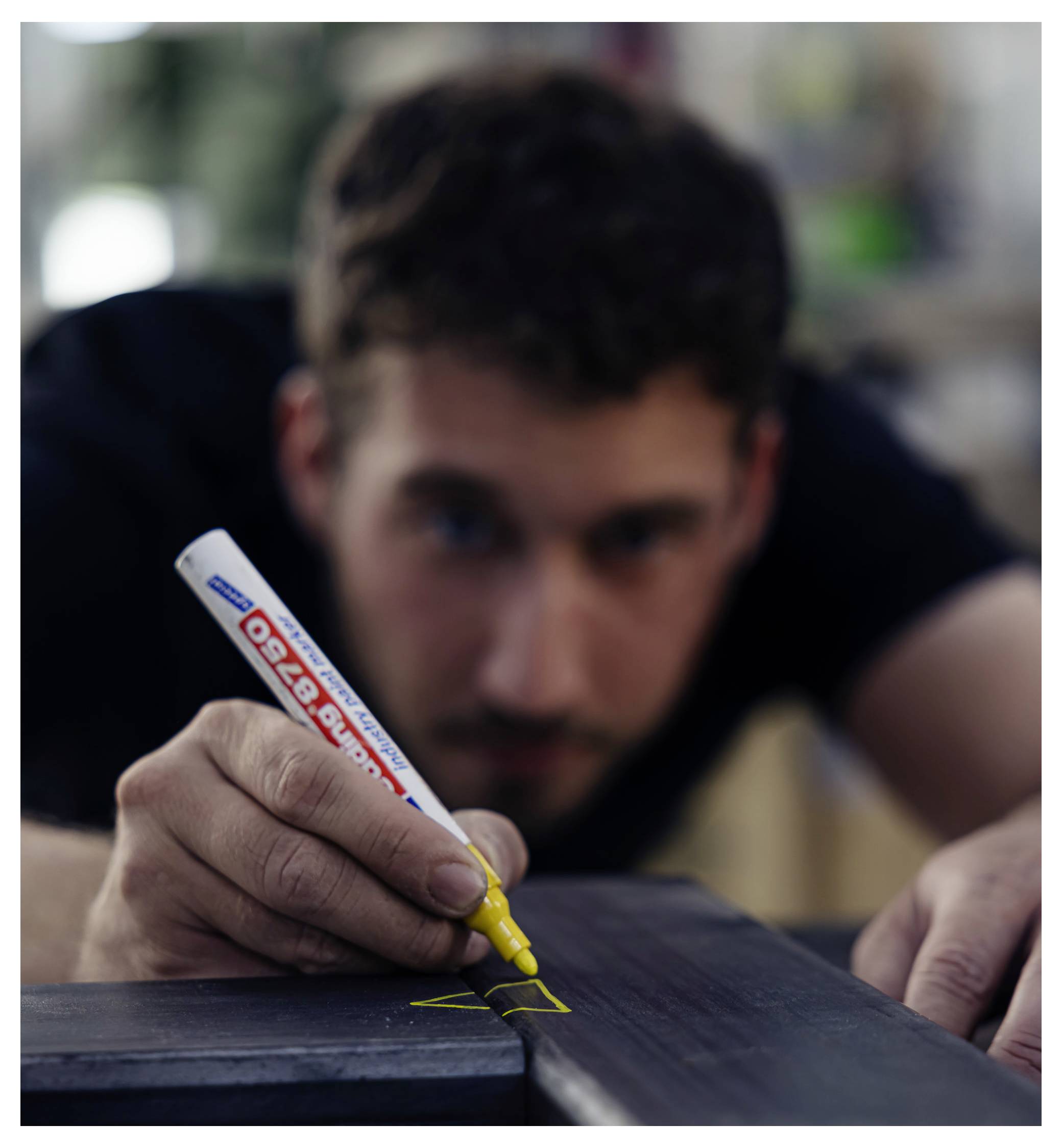 Uomo che usa un pennarello giallo per disegnare su una superficie in legno scuro, concentrato nel marcatura di un bordo o di una giuntura.