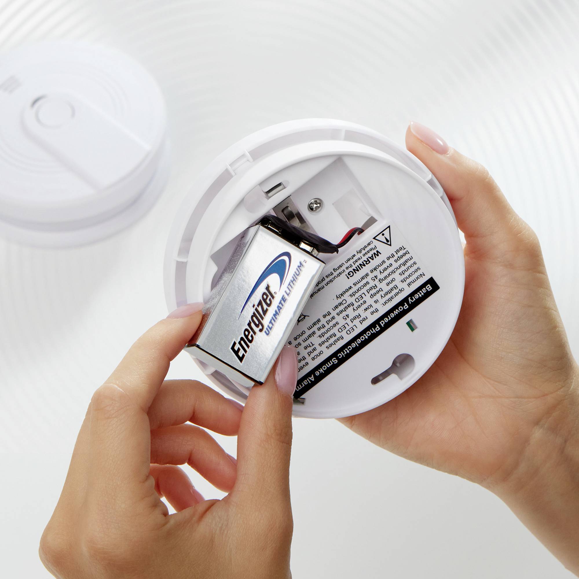 Una persona sta sostituendo la batteria in un rilevatore di fumo. Il marchio della batteria è visibile e il rilevatore di fumo è aperto.