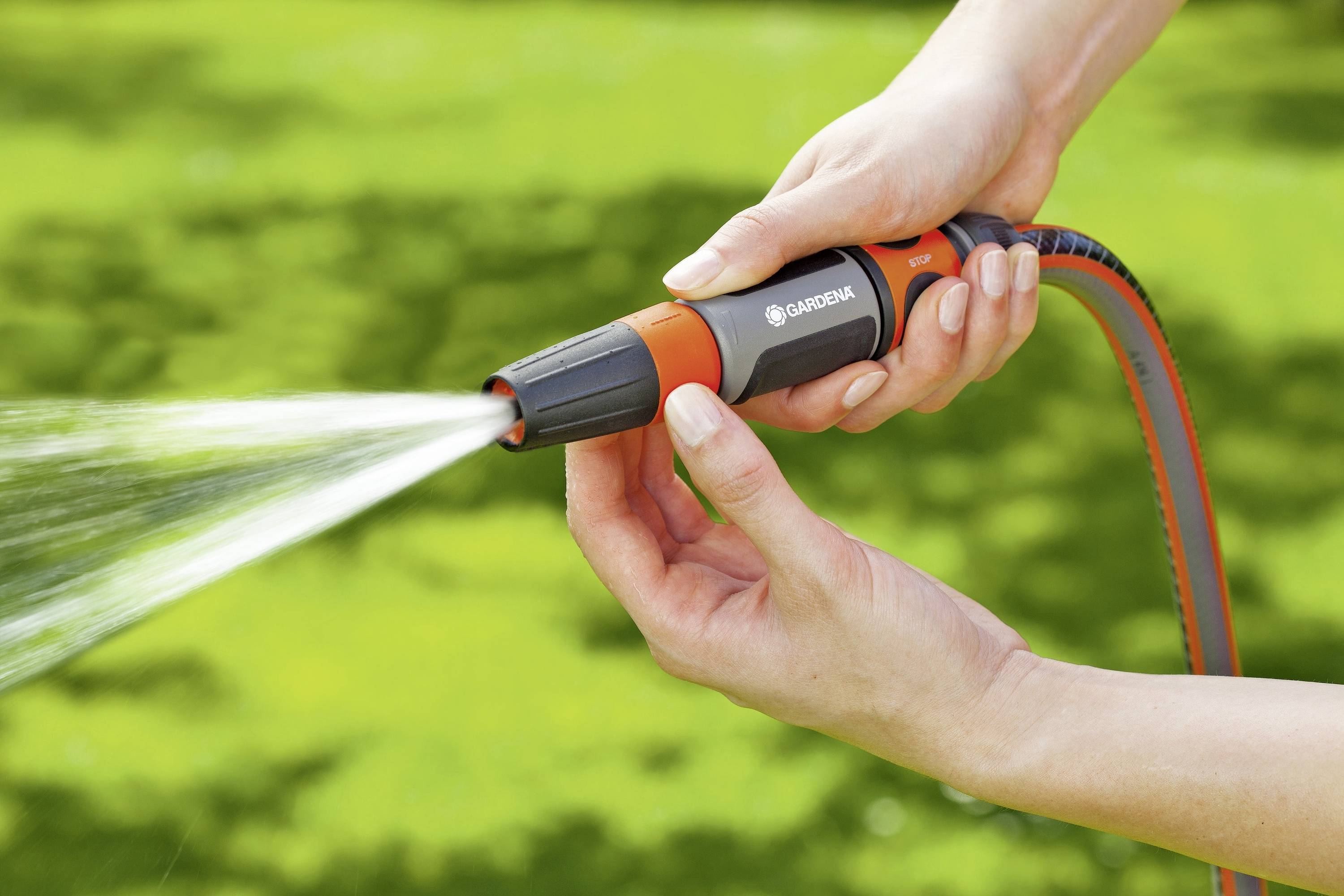 Una persona tiene un tubo da giardino con ugello spray, versa acqua sullo sfondo verde del giardino. Le mani regolano il getto d'acqua.