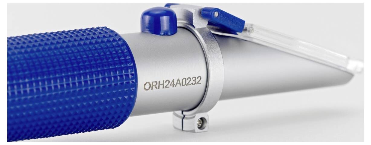 Primo piano di un utensile metallico con impugnatura testurizzata blu e un prisma trasparente in plastica sulla sommità, contrassegnato con 'ORH24A0232'.