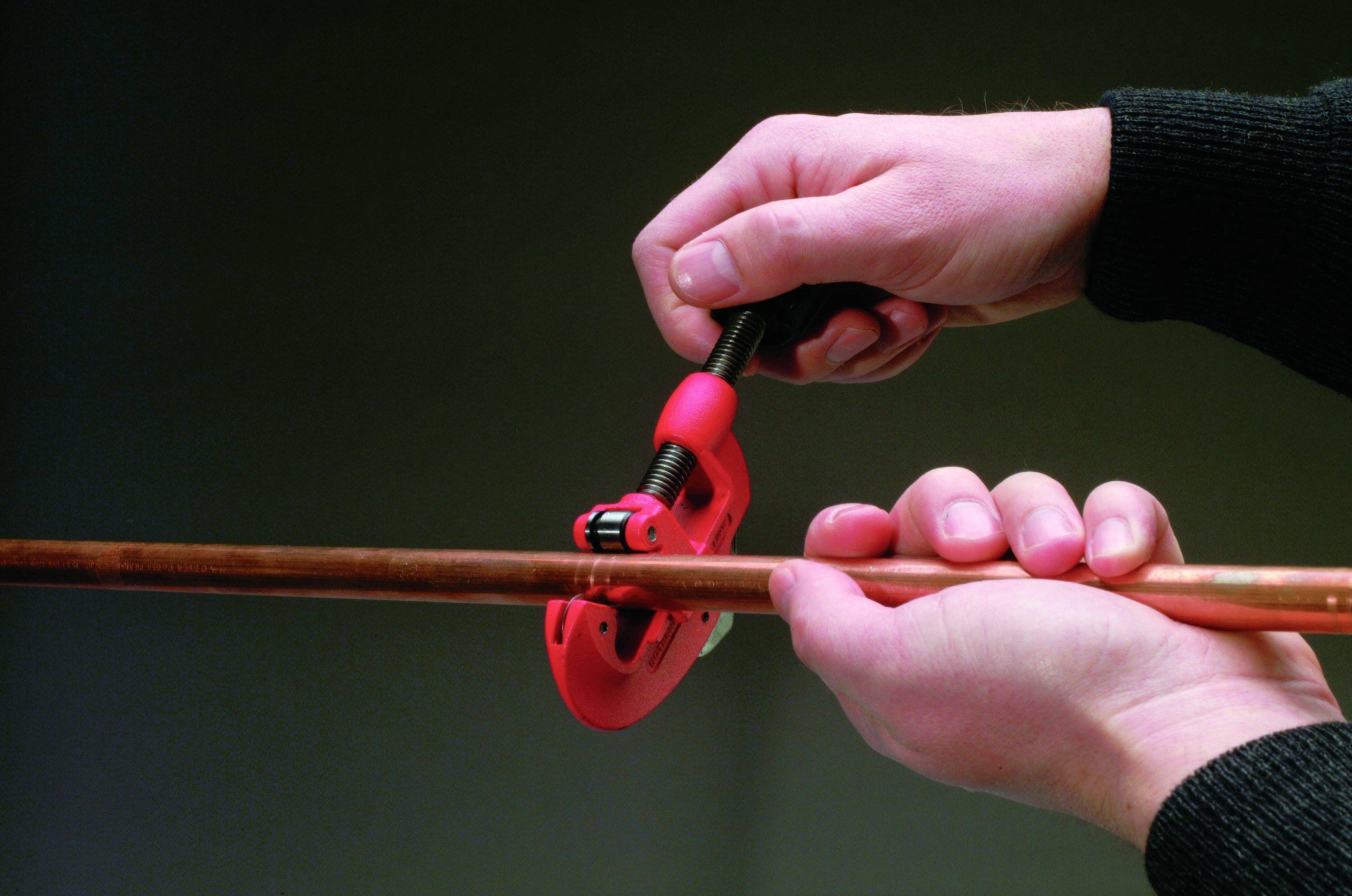 Due mani utilizzano un tagliatubi per tagliare un tubo di rame. Lo sfondo è sfocato per concentrare l'attenzione sull'utensile.