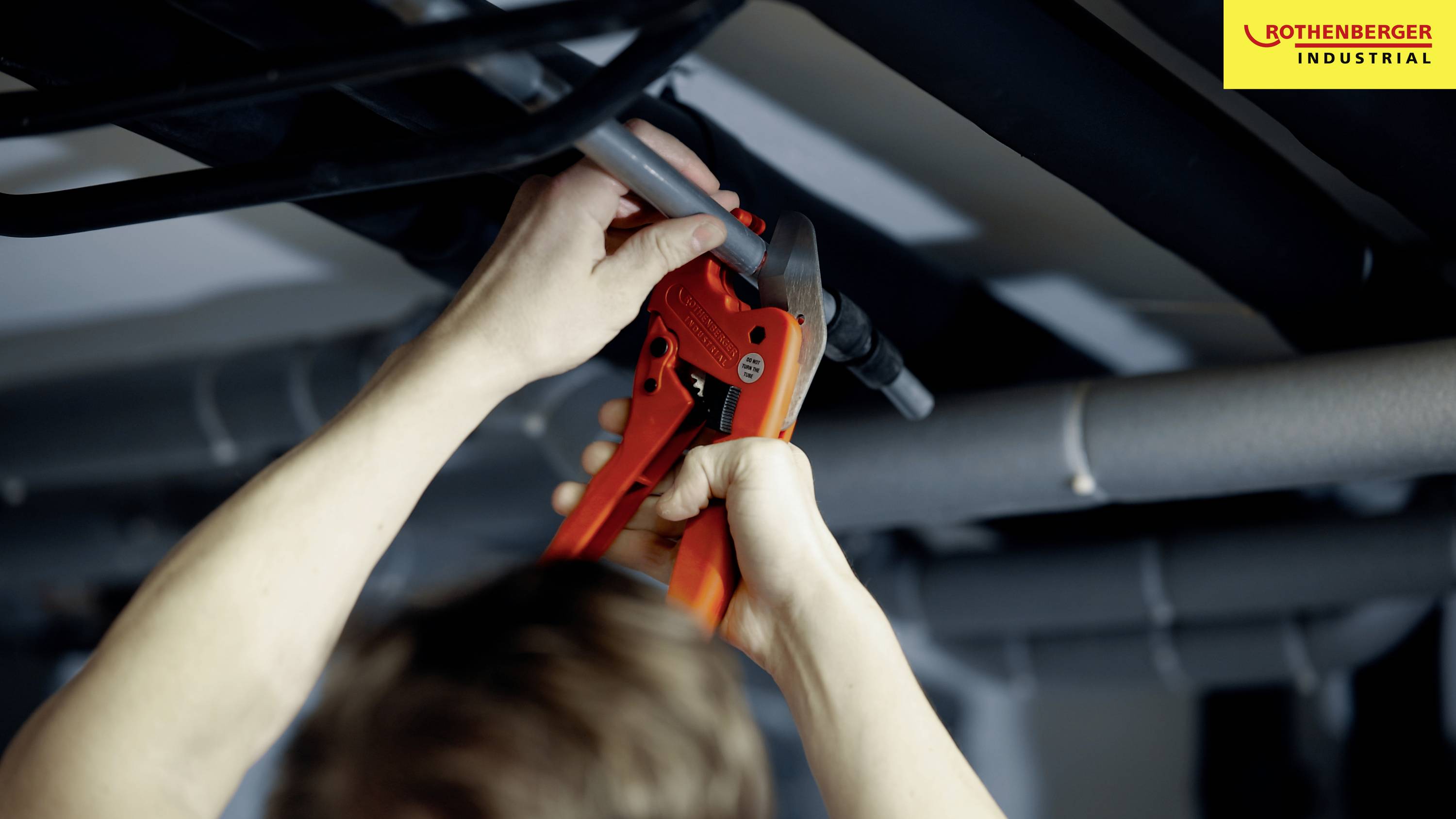 Una persona sta utilizzando un tagliatubi per tagliare un tubo sotto il soffitto. In alto a destra è visibile un logo 'Rothenberger Industrial'.
