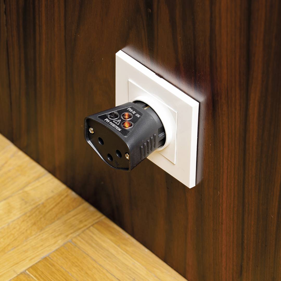 Un tester elettrico è inserito nella presa di una pannellatura in legno. Indica se la connessione elettrica è sicura e corretta.