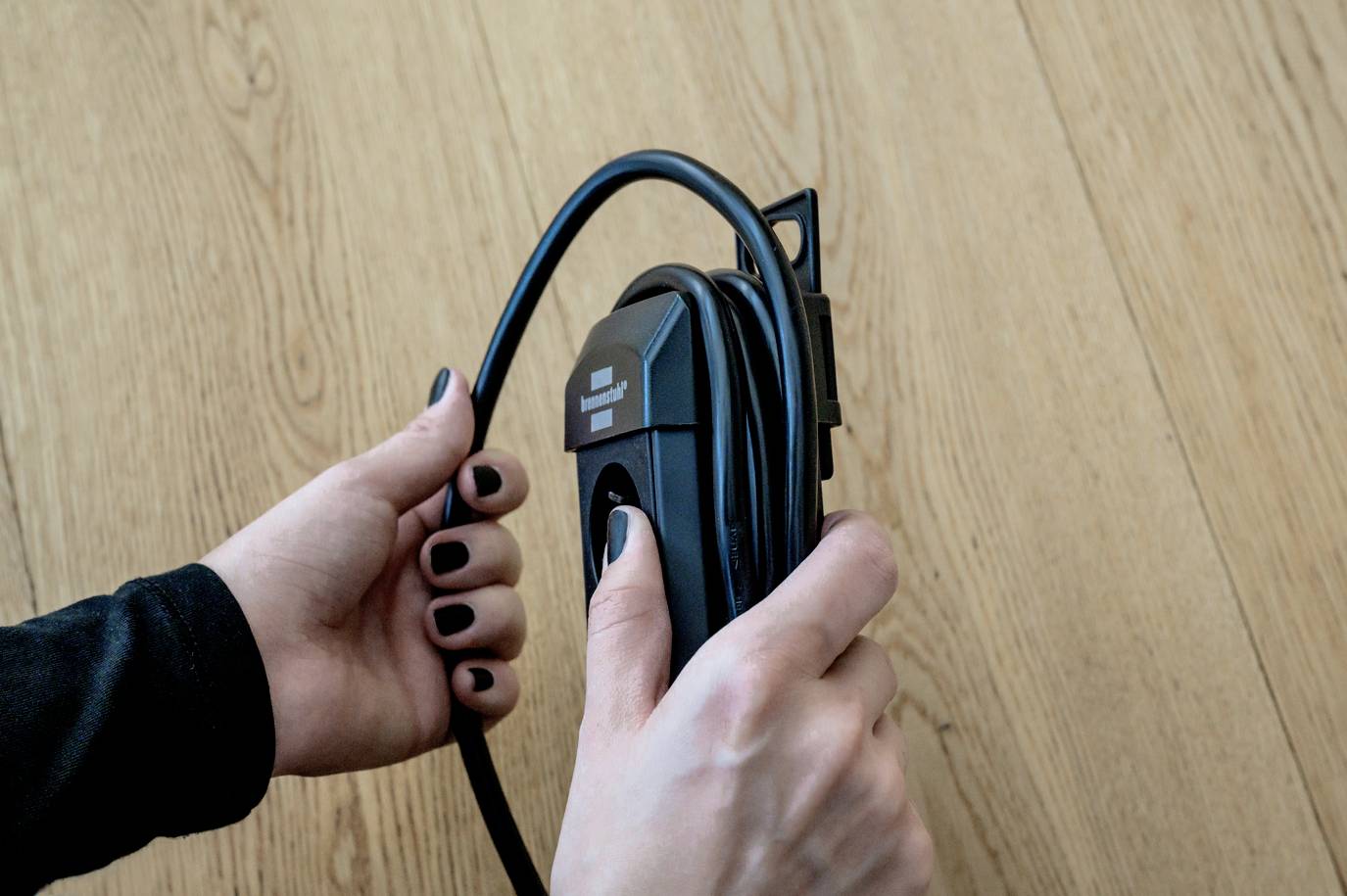 Mani che tengono un cavo di ricarica elettrico contro un pavimento in legno.