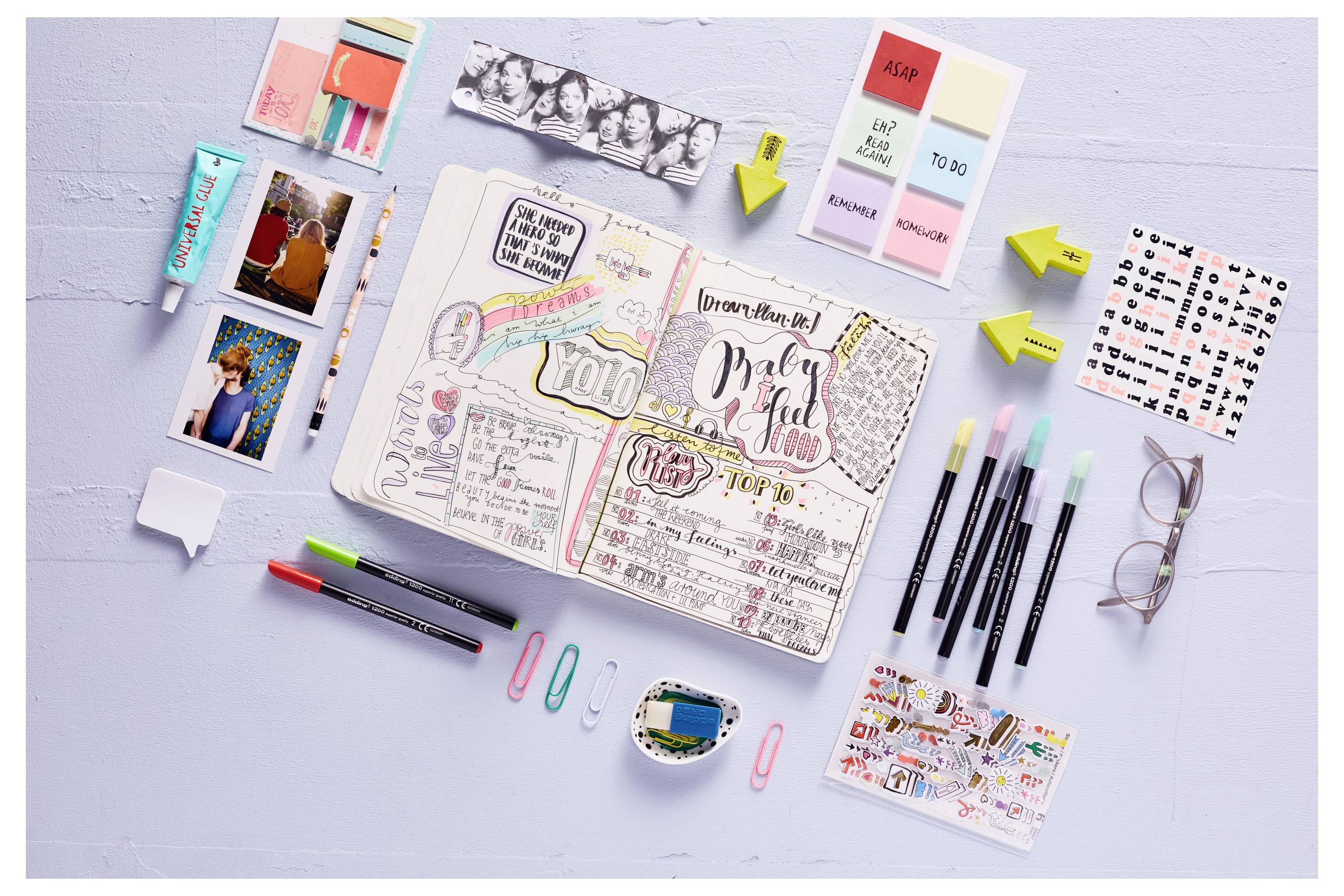 Diffusione di bullet journal aperto con note scritte a mano colorate e lettere "baby shower", circondata da penne, note adesive, foto, clip e adesivi.