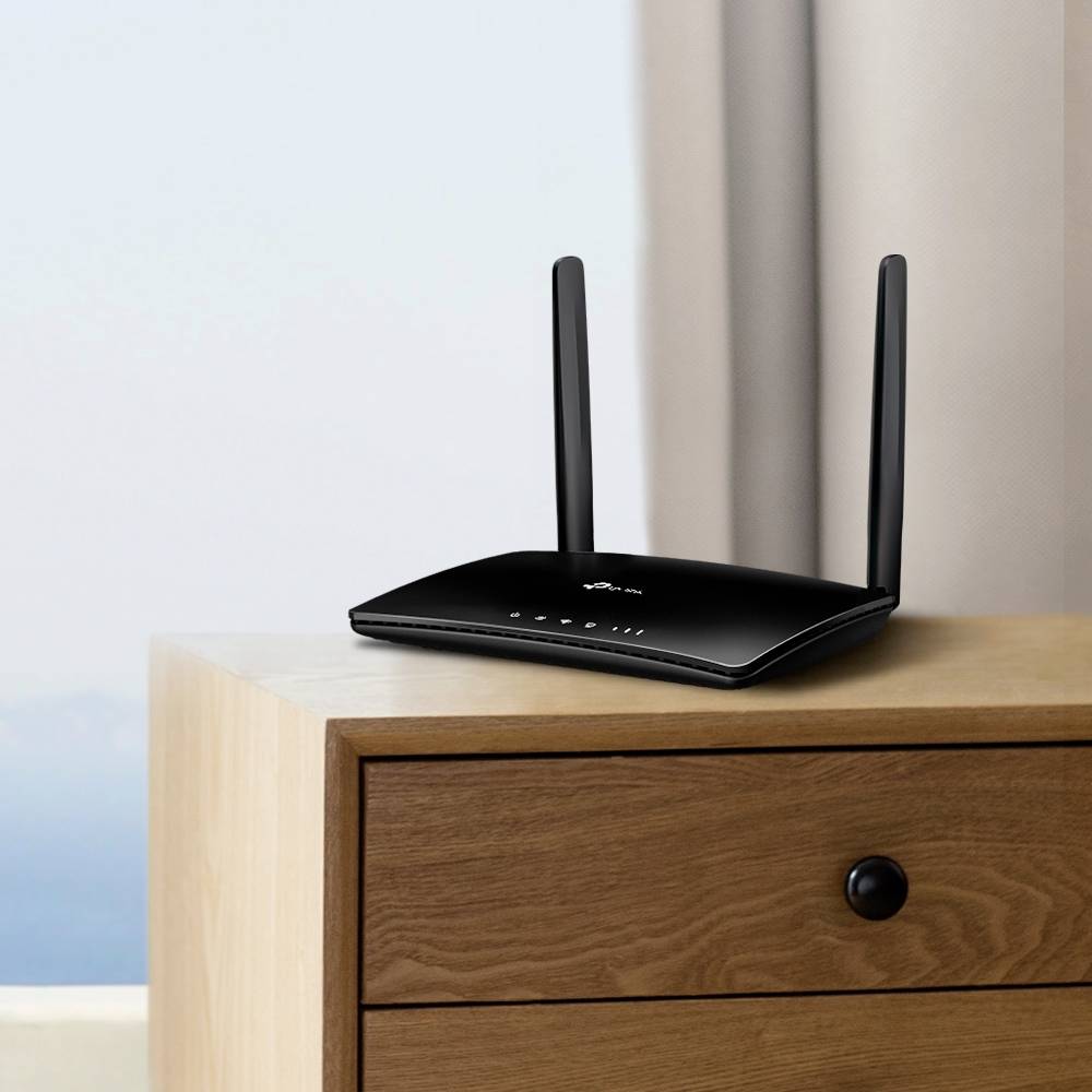 Un router wireless nero con due antenne è posizionato su un cassettone di legno. Sullo sfondo si intravede una parete blu sfocata.