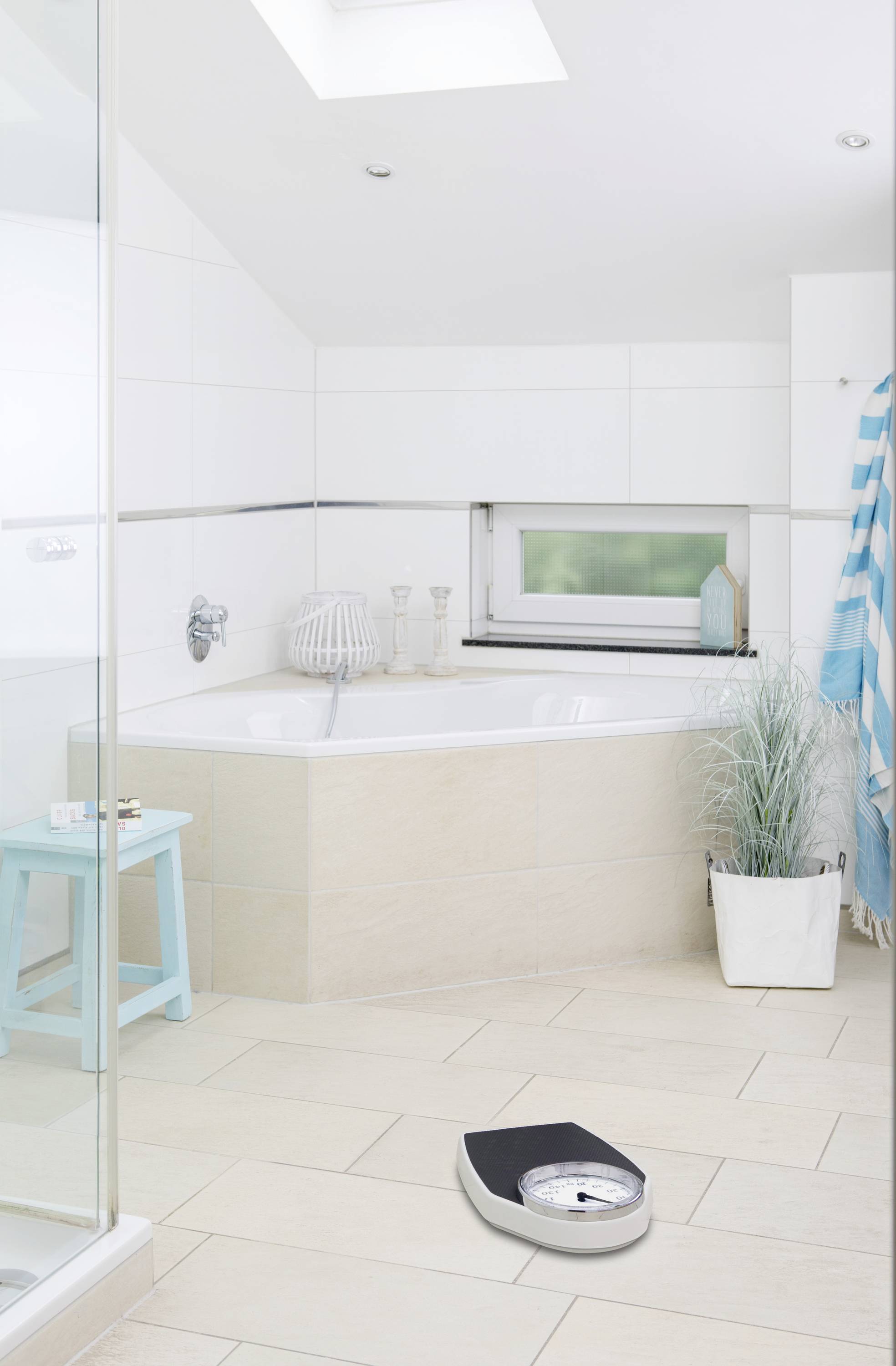 Bagno moderno con vasca da bagno, finestra, accenti blu, pianta in vaso e bilancia personale sul pavimento.