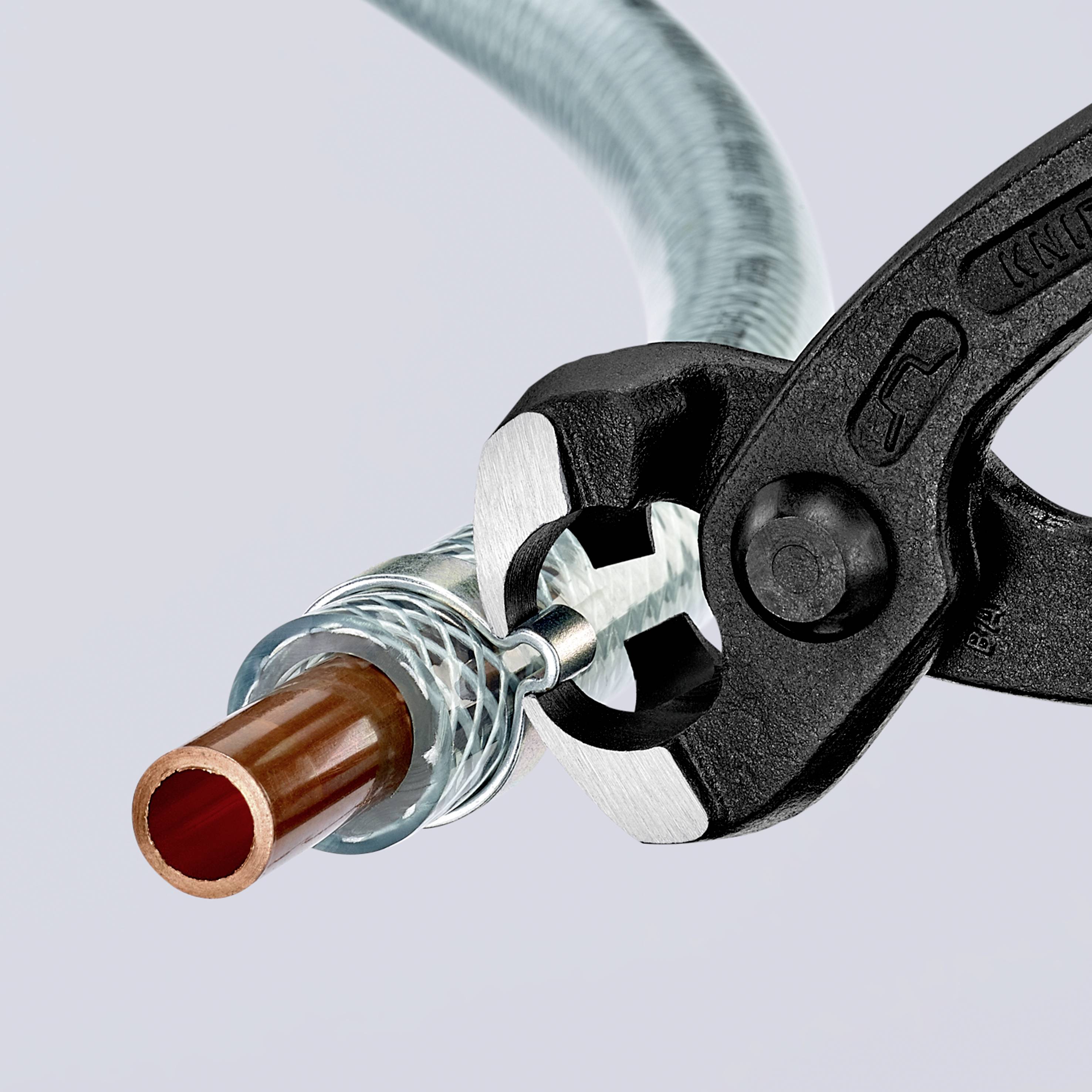Un tagliatubi sta tagliando un tubo di rame. L'utensile è bloccato saldamente sul tubo, che è parte di un tubo flessibile.
