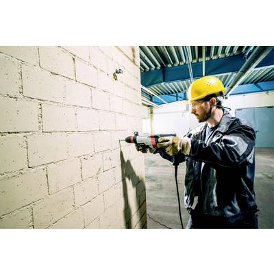 Un muratore indossa un casco giallo e utilizza un trapano per forare un muro interno in mattoni.