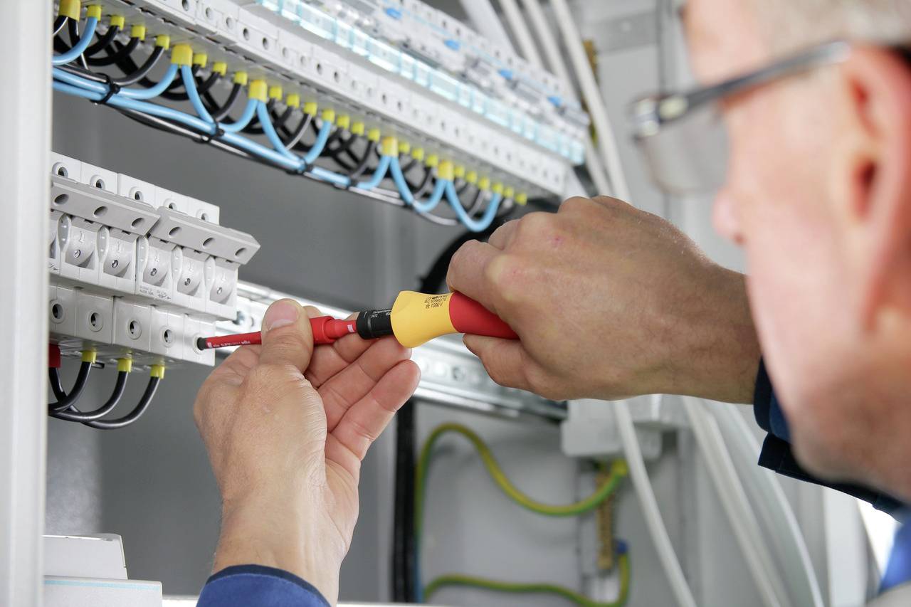 Un elettricista lavora con un cacciavite su un quadro elettrico per installare o manutenere connessioni elettriche.