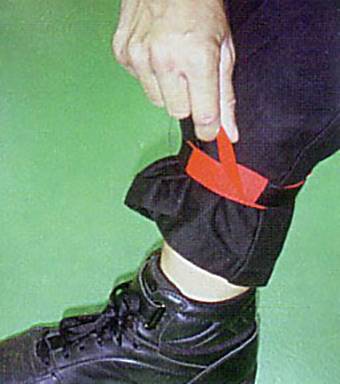 Una persona tira un nastro rosso che è arrotolato intorno alla propria gamba del pantalone, indossando una scarpa nera.