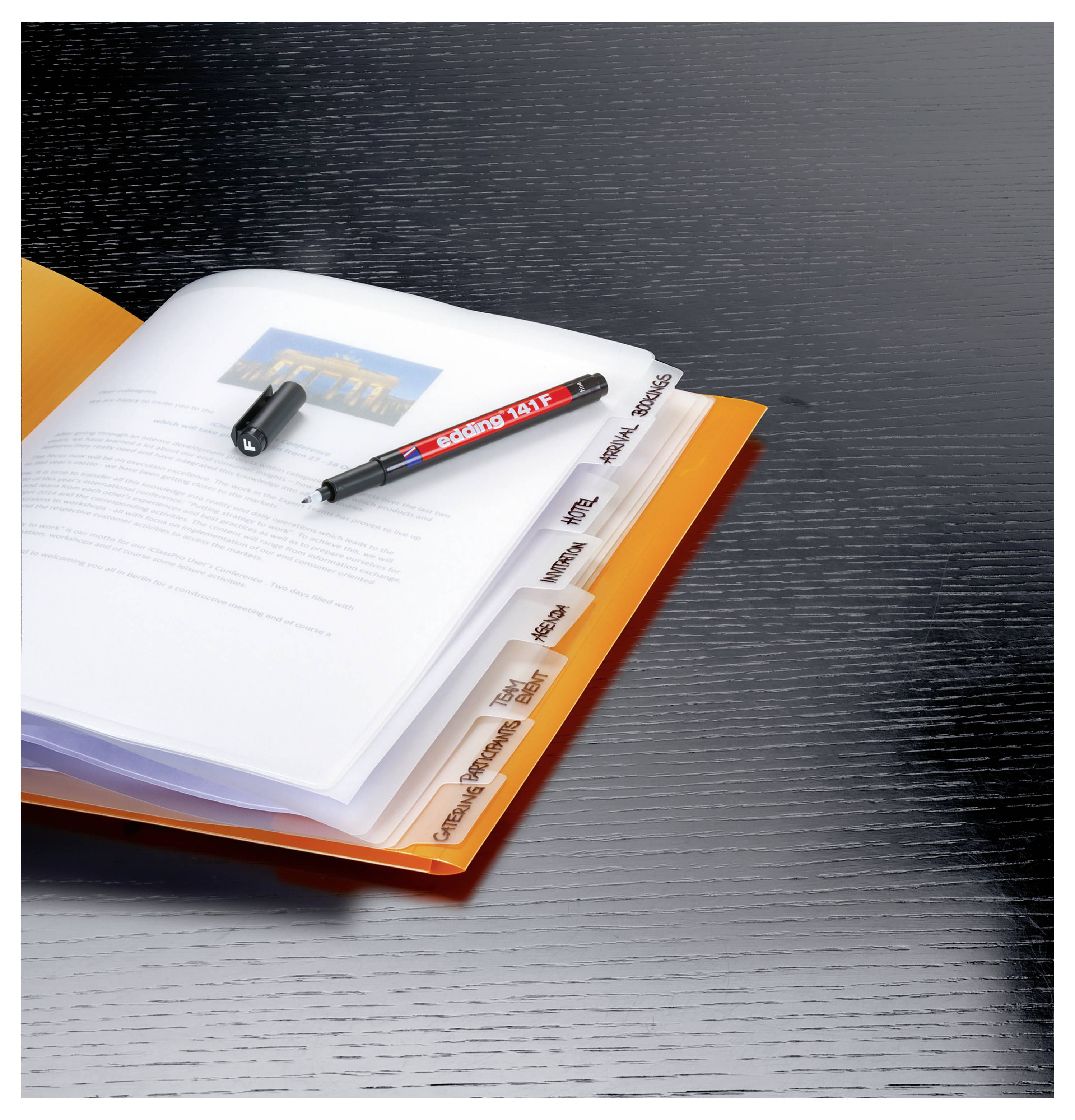Raccoglitore arancione aperto con pagine a schede su una scrivania scura, con una penna e un cappuccio sopra; un documento stampato si trova all'interno.