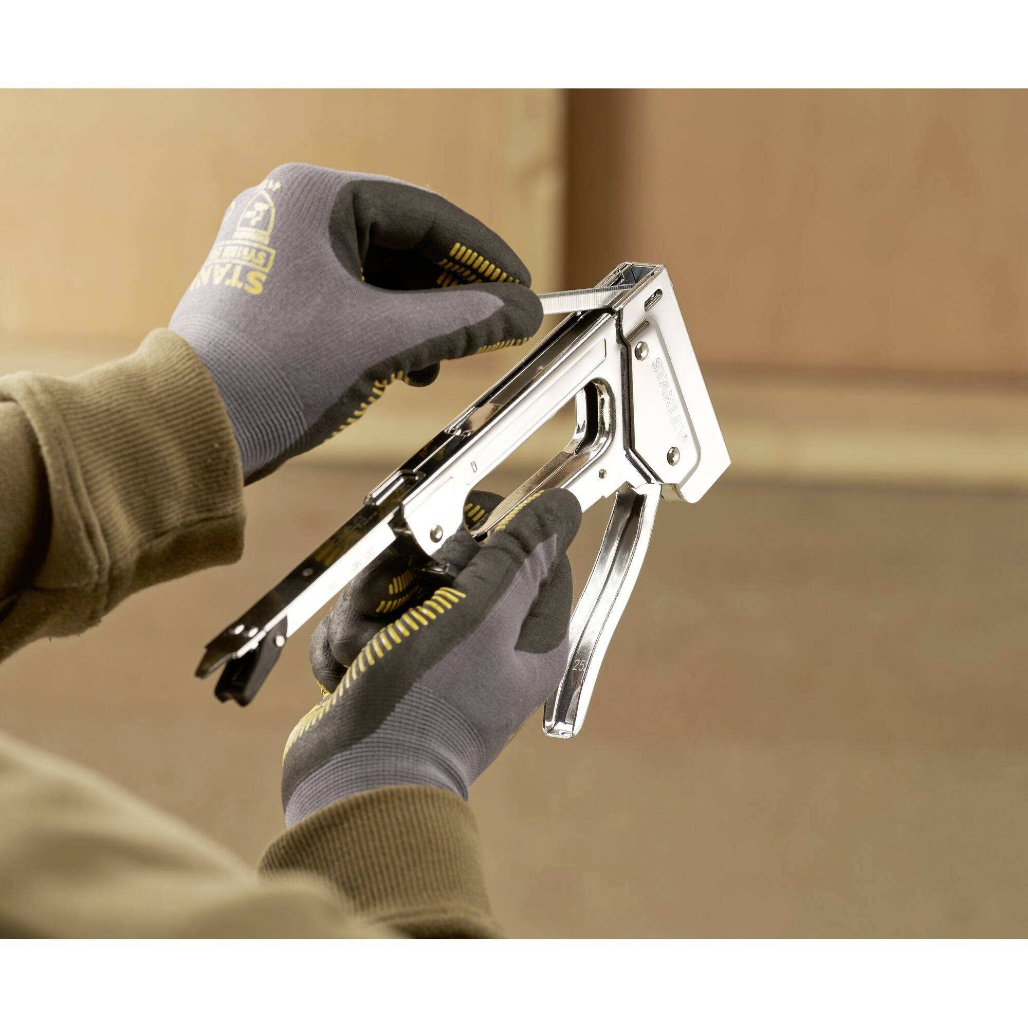 'Primo piano di mani che tengono e utilizzano un tacker manuale, probabilmente per fissare materiali su una superficie di legno.'