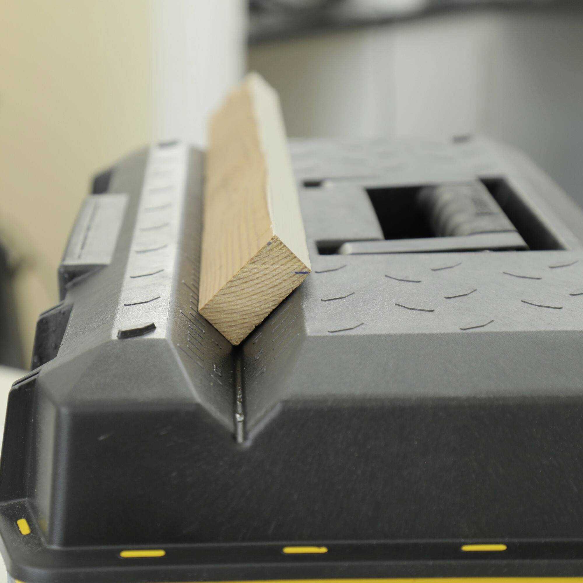 Macchina da taglio con un pezzo di legno sul tavolo, pronta per segare. Sfondo sfocato, con messa a fuoco sul legno e sulla macchina.