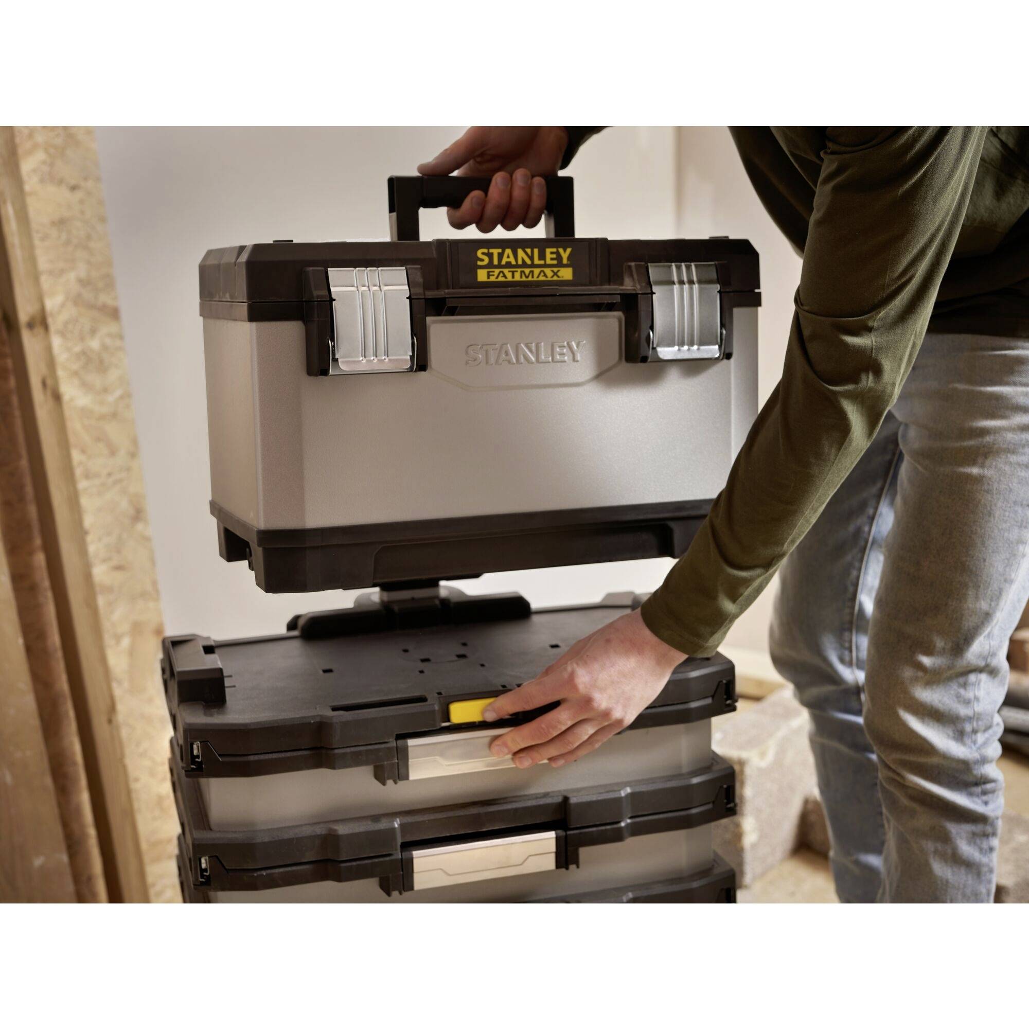 Una persona sta impilando un contenitore degli attrezzi argentato con manico nero su diversi contenitori di plastica trasparenti in un laboratorio.