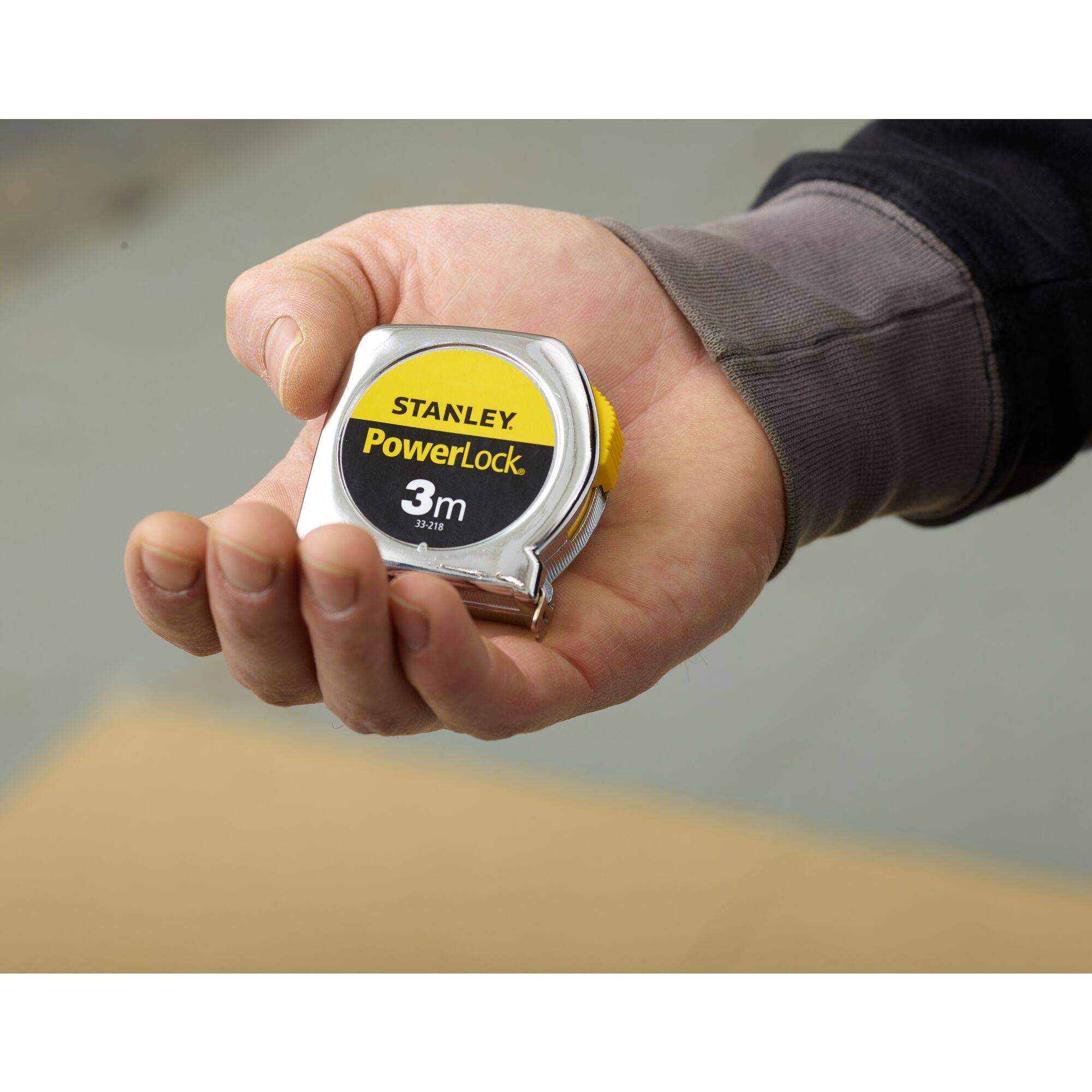 Una mano tiene un nastro metrico con la scritta 'Stanley PowerLock 3m'.