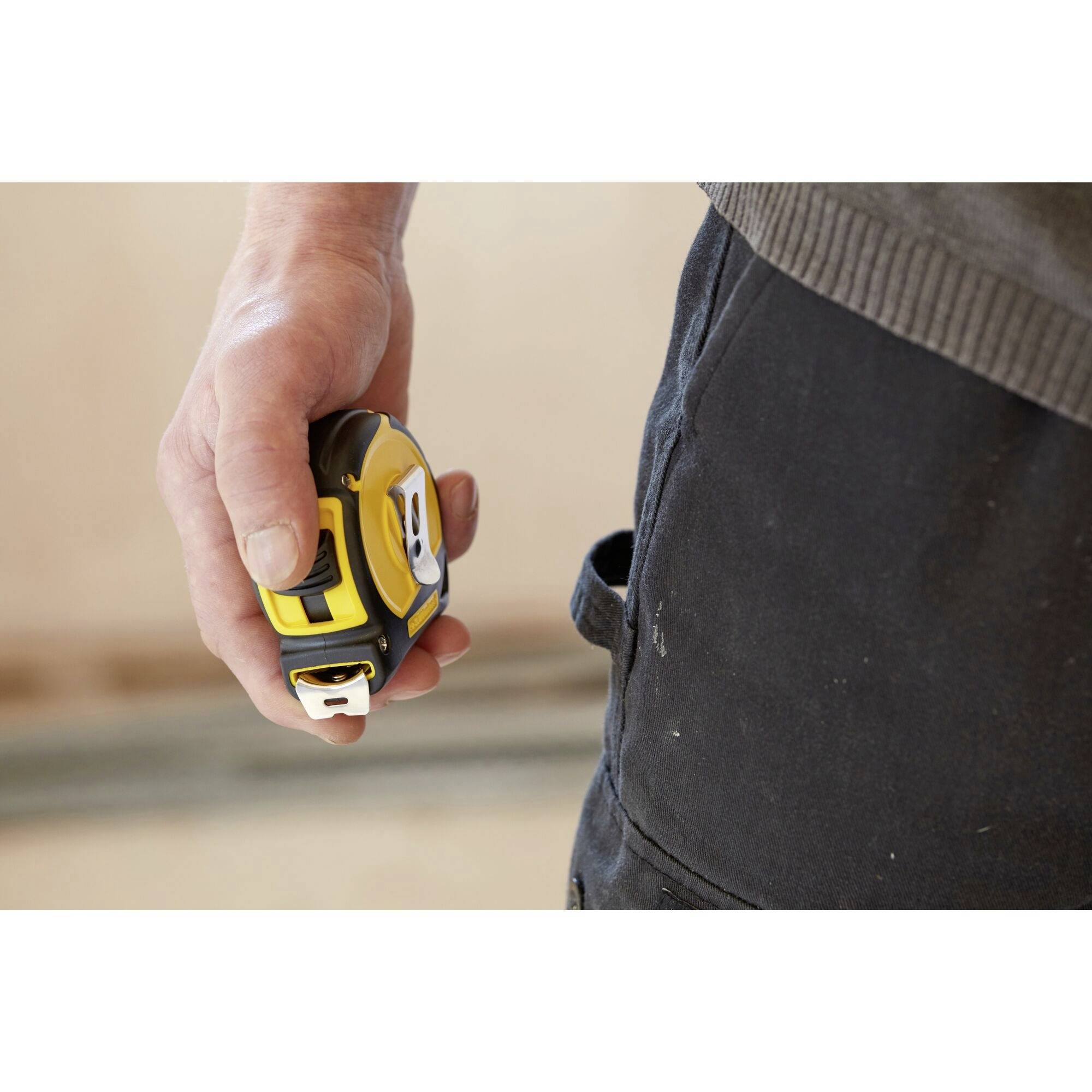 Una persona tiene in mano un metro a nastro giallo e nero, pronto per essere utilizzato, probabilmente per un lavoro edile o di ristrutturazione.