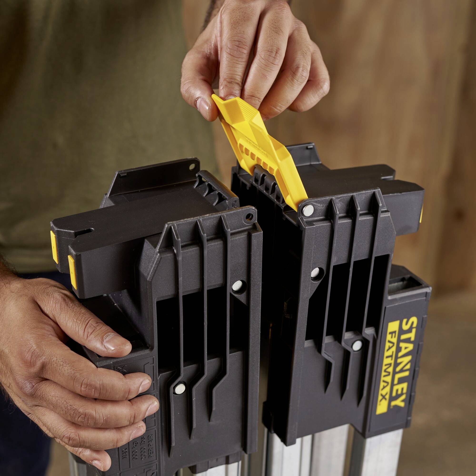 Una persona sta utilizzando un attrezzo giallo per fissare un telaio pieghevole nero con la scritta 'STANLEY FATMAX'.