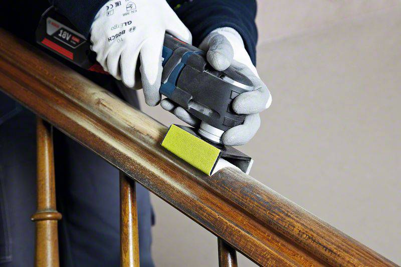Una persona sta utilizzando una levigatrice elettrica per levigare una ringhiera in legno. Indossa guanti protettivi.