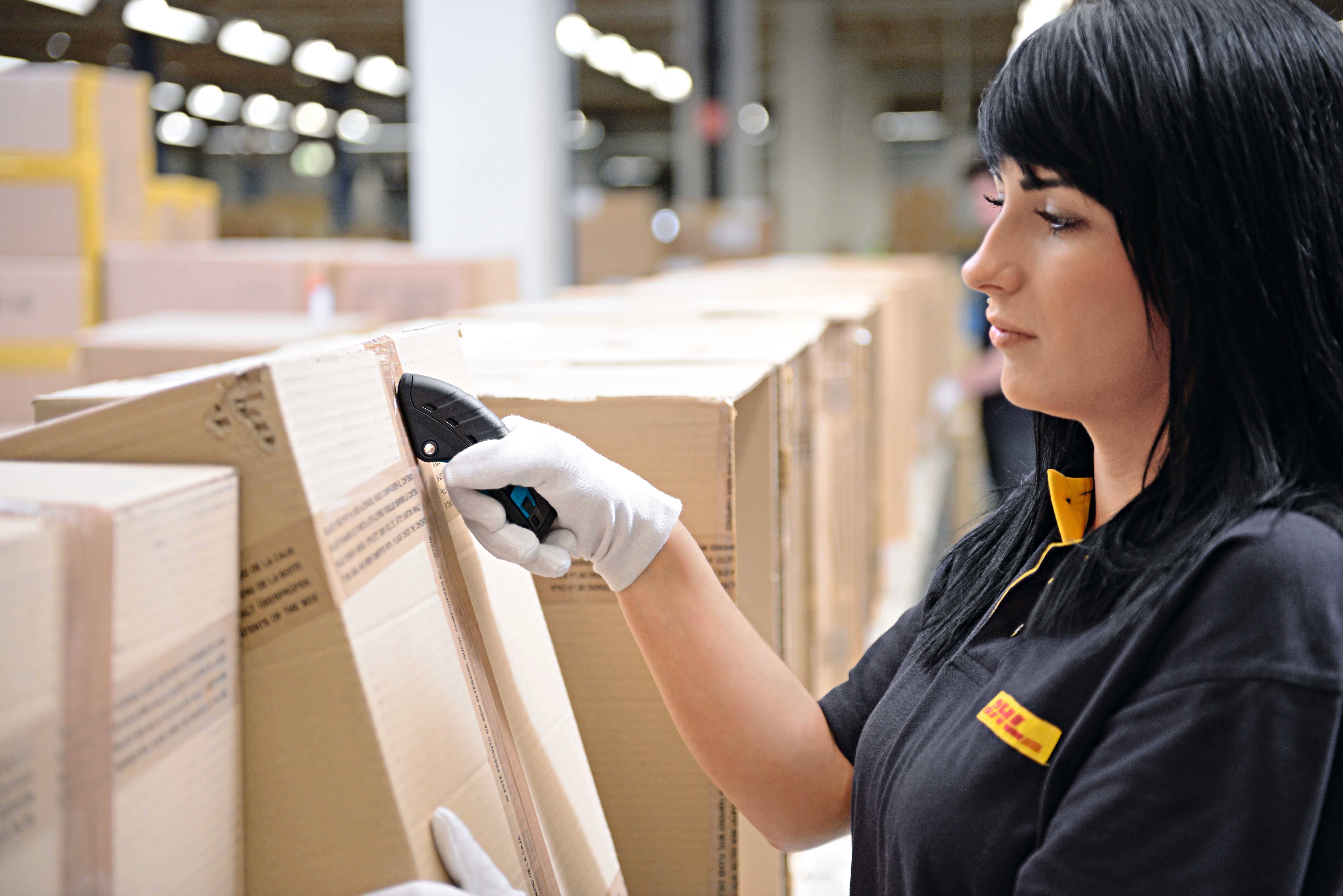 Una donna in abbigliamento da lavoro utilizza uno scanner per leggere i codici a barre su scatole impilate in un magazzino.