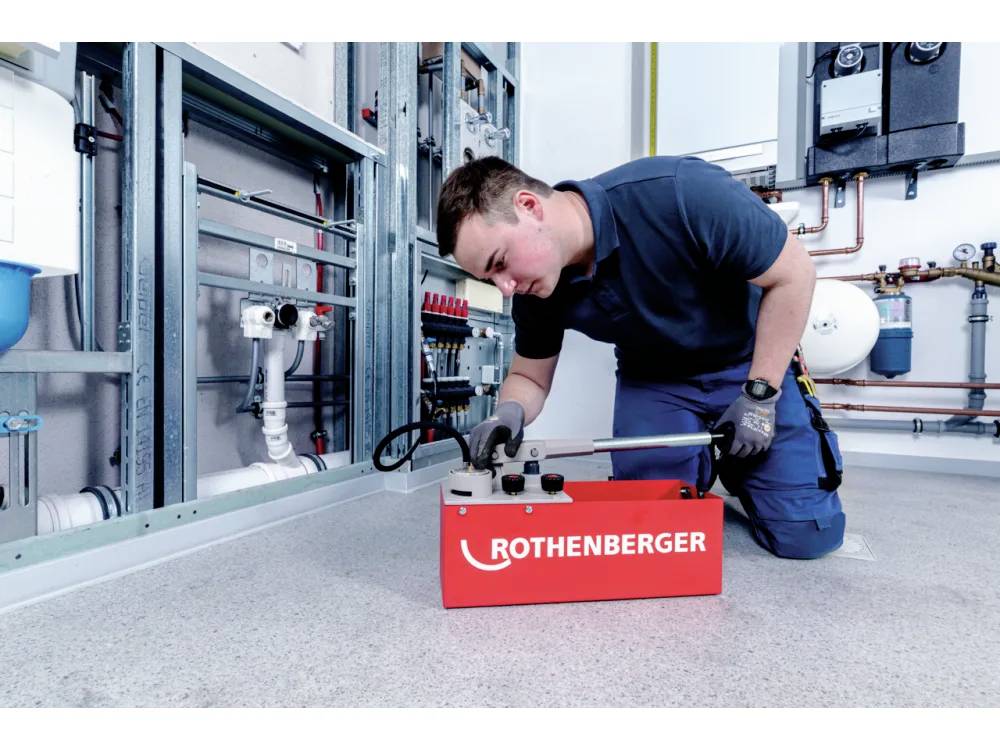 Una persona sta utilizzando un attrezzo da una custodia rossa 'ROTHENBERGER' in un locale tecnico con vari tubi e attrezzature sulle pareti.