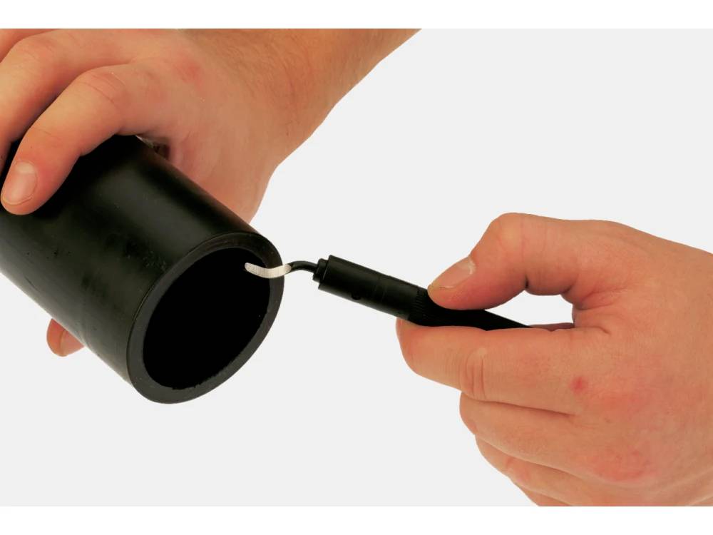Mani che reggono un tubo cilindrico nero, con una mano che utilizza uno strumento per svasare per rimuovere i bordi ruvidi dall'estremità tagliata.