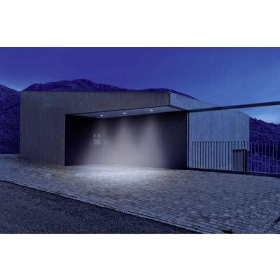Un edificio moderno con forme squadrate al crepuscolo. Una fonte luminosa illumina l'ingresso. Montagne sono visibili sullo sfondo.