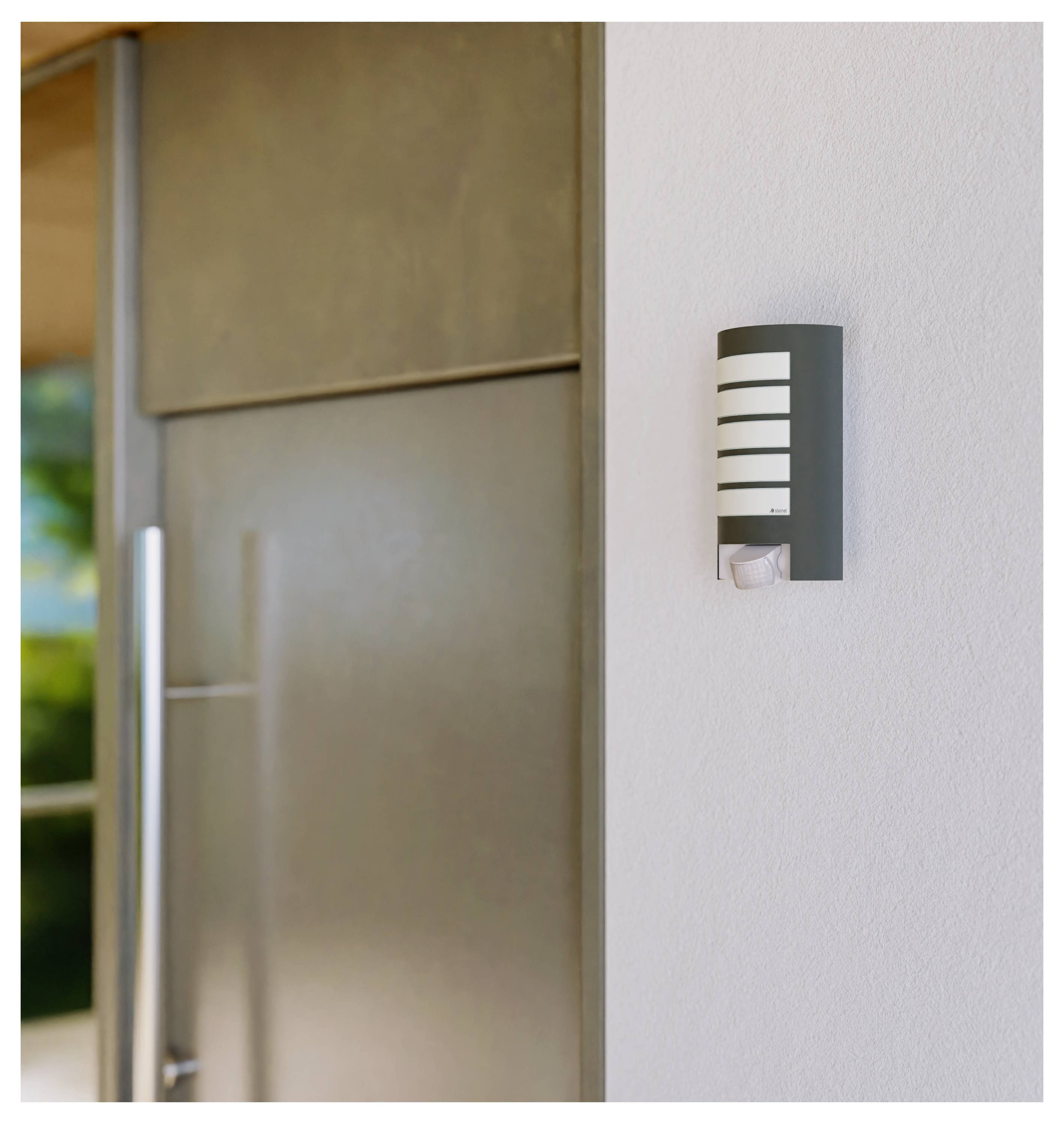 Plafoniera esterna montata a parete accanto a una porta in vetro su un muro esterno bianco.