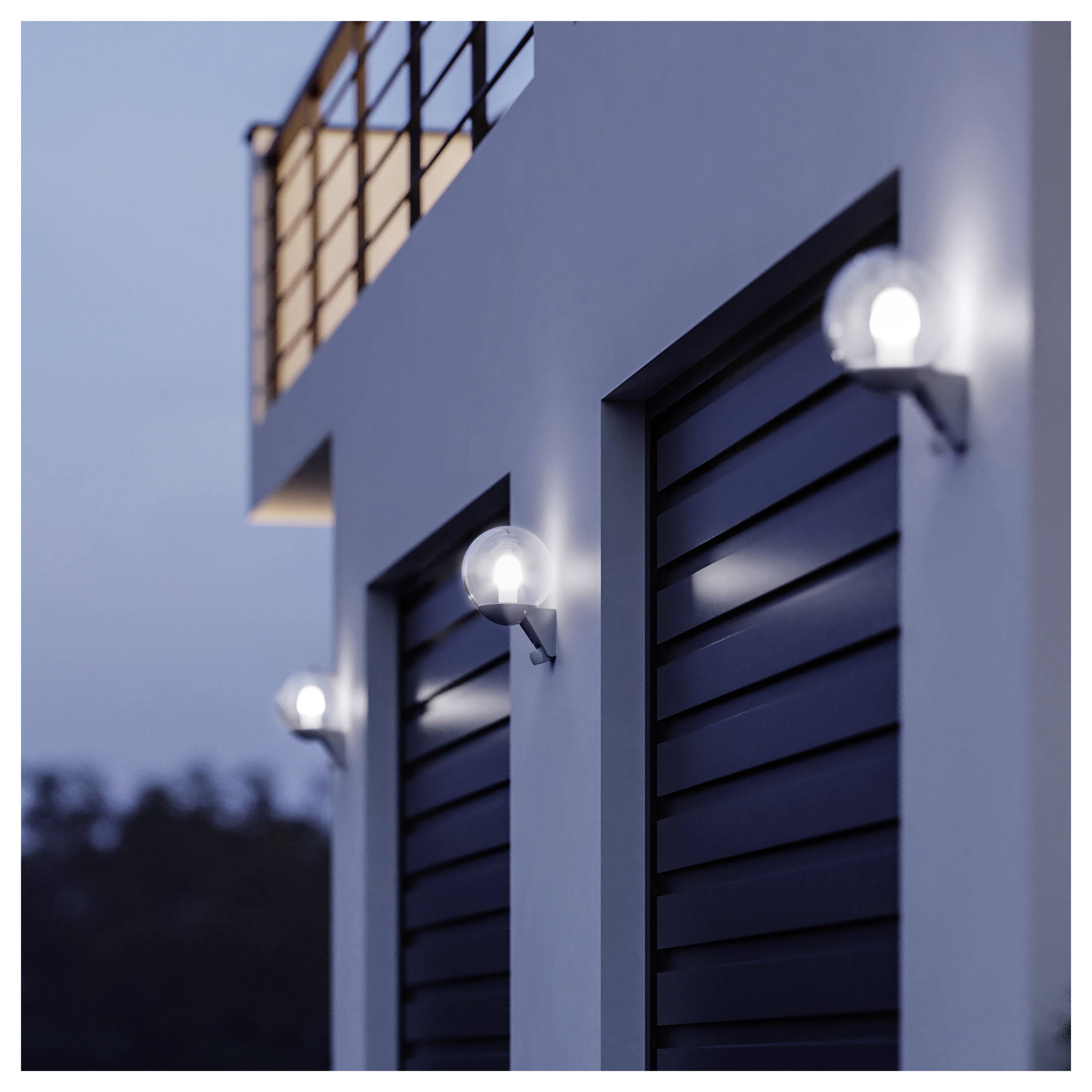 Esterno di edificio bianco moderno con persiane nere a lamelle e applique murali che si illuminano al tramonto