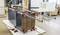 In un laboratorio viene assemblato un armadio. Grandi morsetti tengono ferme delle tavole di legno scuro. Una persona lavora sullo sfondo.