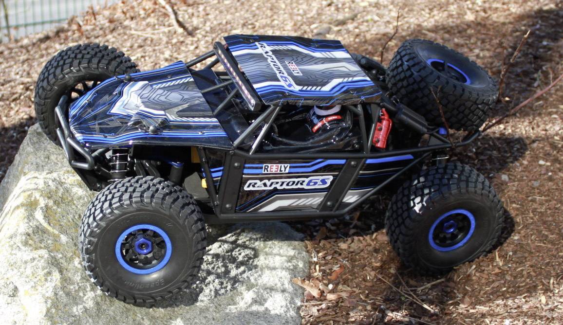 Un'auto telecomandata con pneumatici robusti e design blu-nero guida su un terreno roccioso all'aperto.