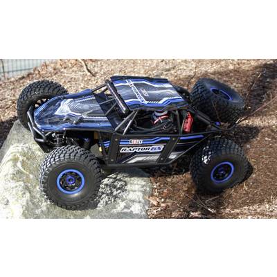 Un'auto telecomandata con pneumatici robusti e design blu-nero guida su un terreno roccioso all'aperto.