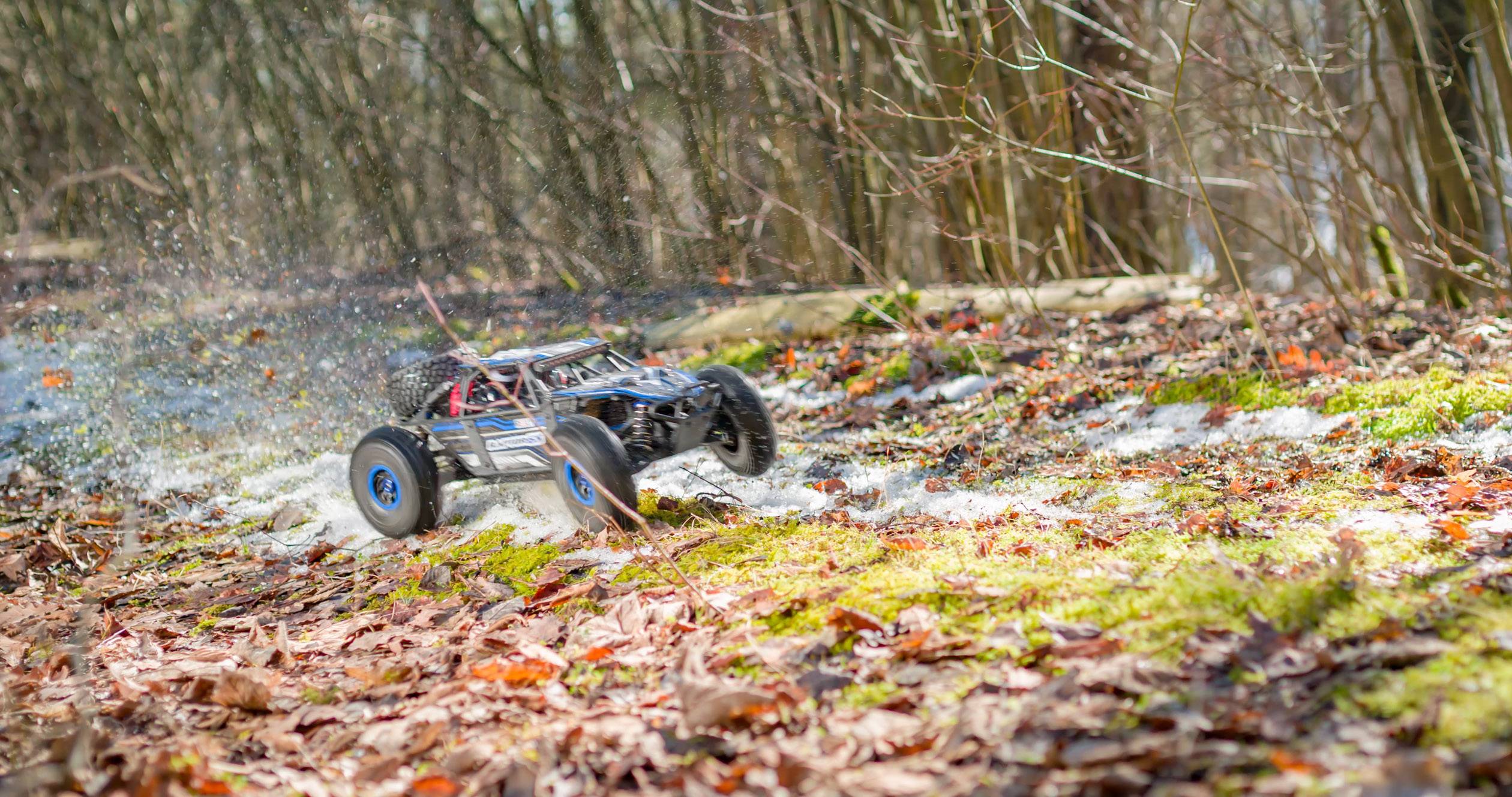 Un'auto radiocomandata sfreccia ad alta velocità attraverso un bosco autunnale, sollevando foglie e terra.