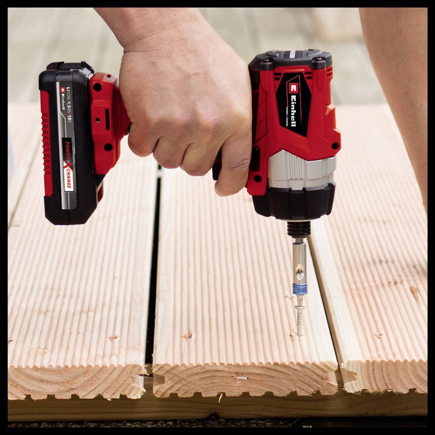 Una mano tiene un avvitatore a batteria senza fili sopra una superficie in legno, pronta a serrare una vite.