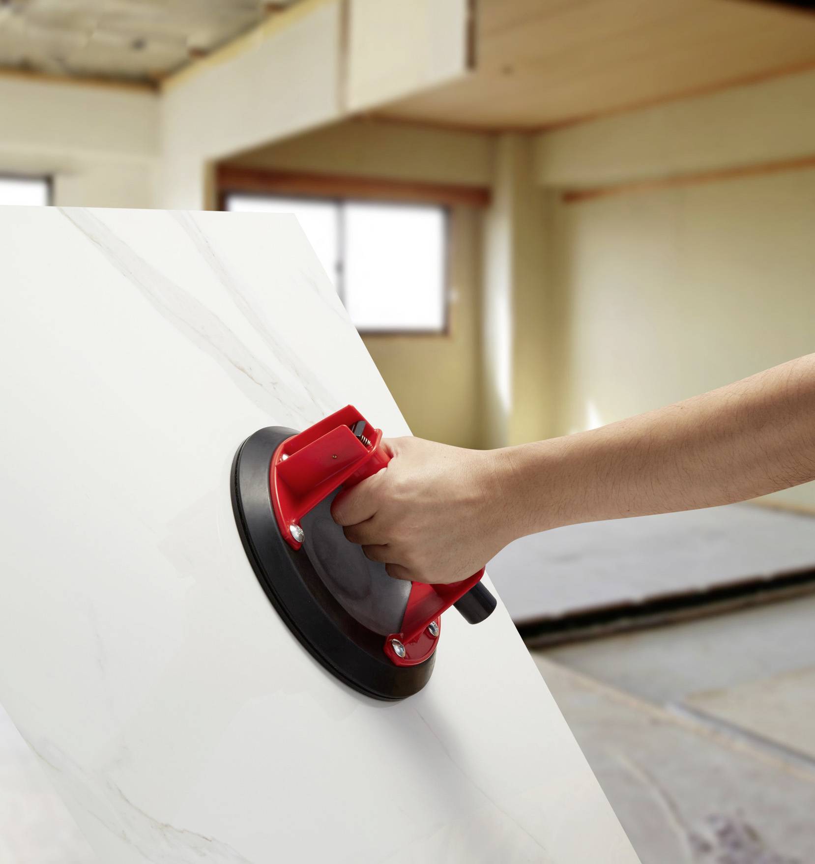 Una mano tiene un ventosa rosso su una grande piastra di ceramica all'interno di un ambiente. Sullo sfondo sono visibili delle finestre.