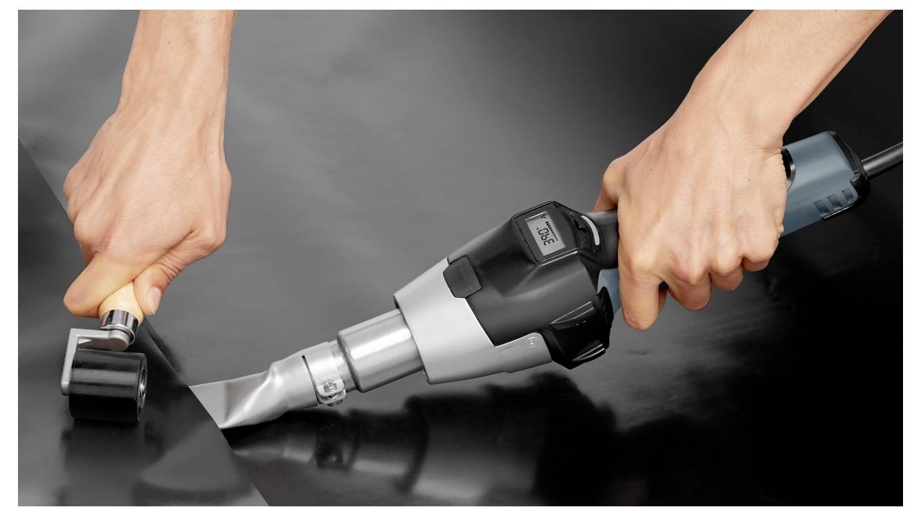 Mani che azionano un utensile da taglio elettrico con una lama su una superficie nera, rifinendo una cucitura o bordo del materiale.