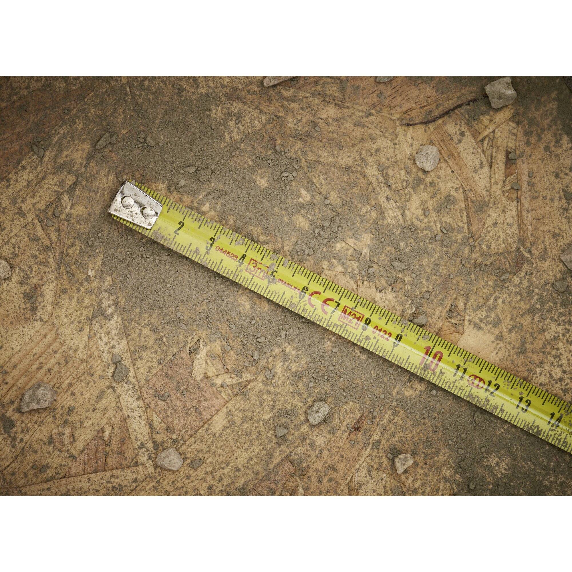 Un nastro metrico giallo è posizionato su un sfondo terroso con piccoli sassi sparsi. Il nastro metrico mostra circa 15 centimetri.