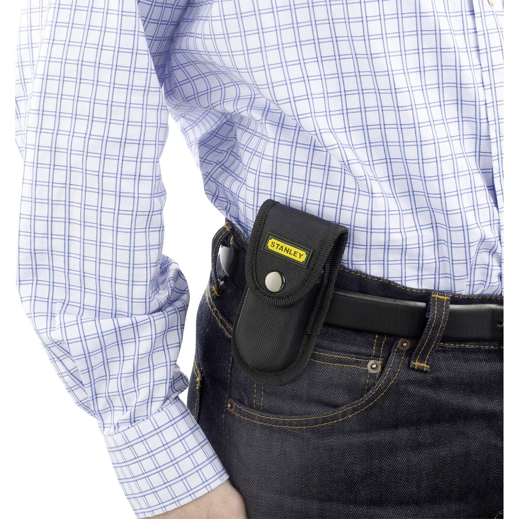 Una persona indossa una camicia a quadri e una borsa nera con il logo 'Stanley' agganciata alla cintura.