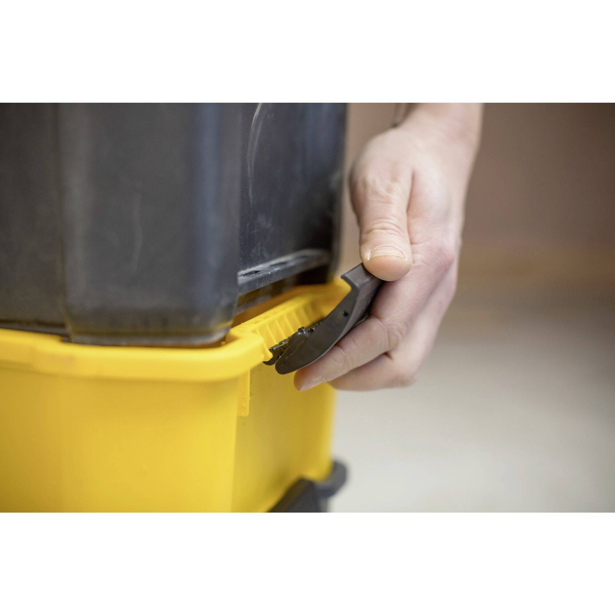 Una mano utilizza un attrezzo nero per chiudere in modo sicuro un contenitore giallo con un coperchio nero.