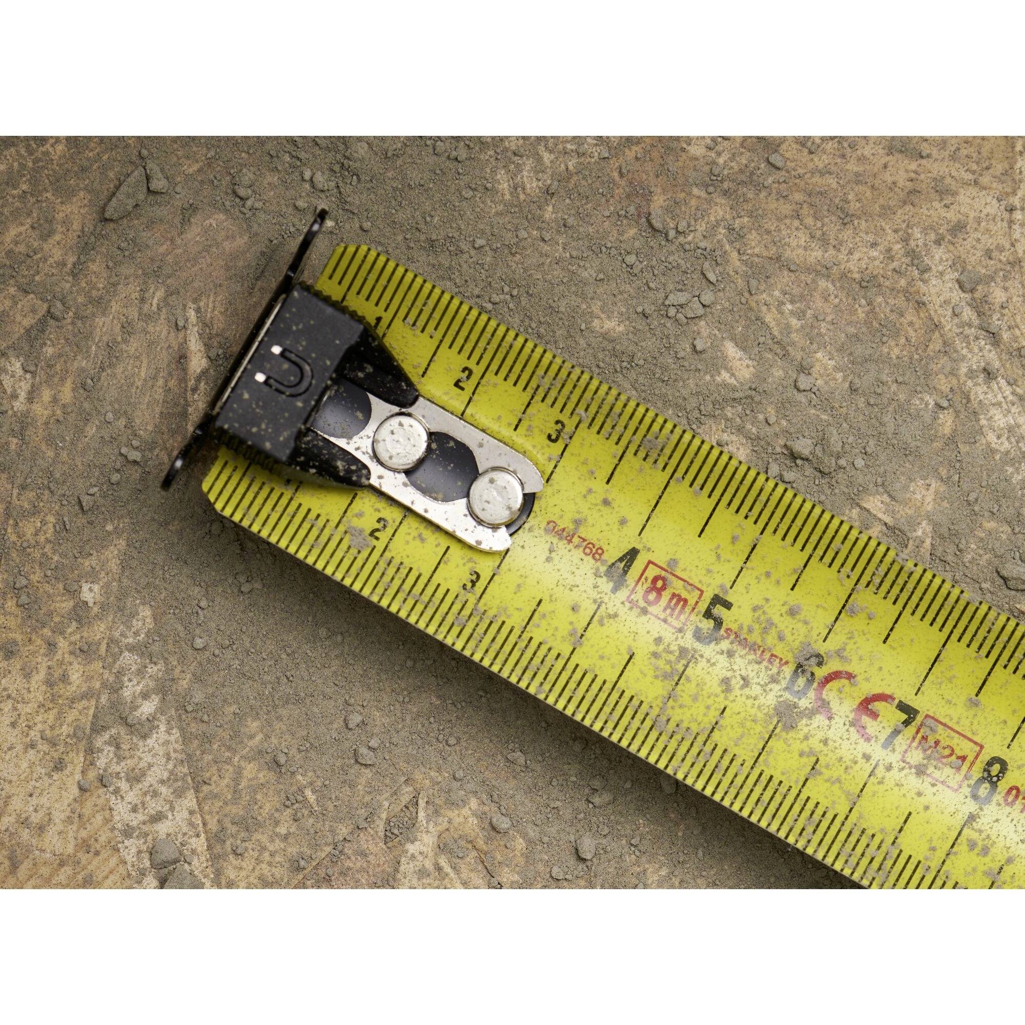 Un nastro metrico è aperto su un terreno sabbioso, i numeri sono indicati in centimetri, sono visibili le marcature da 1 a 5 cm.