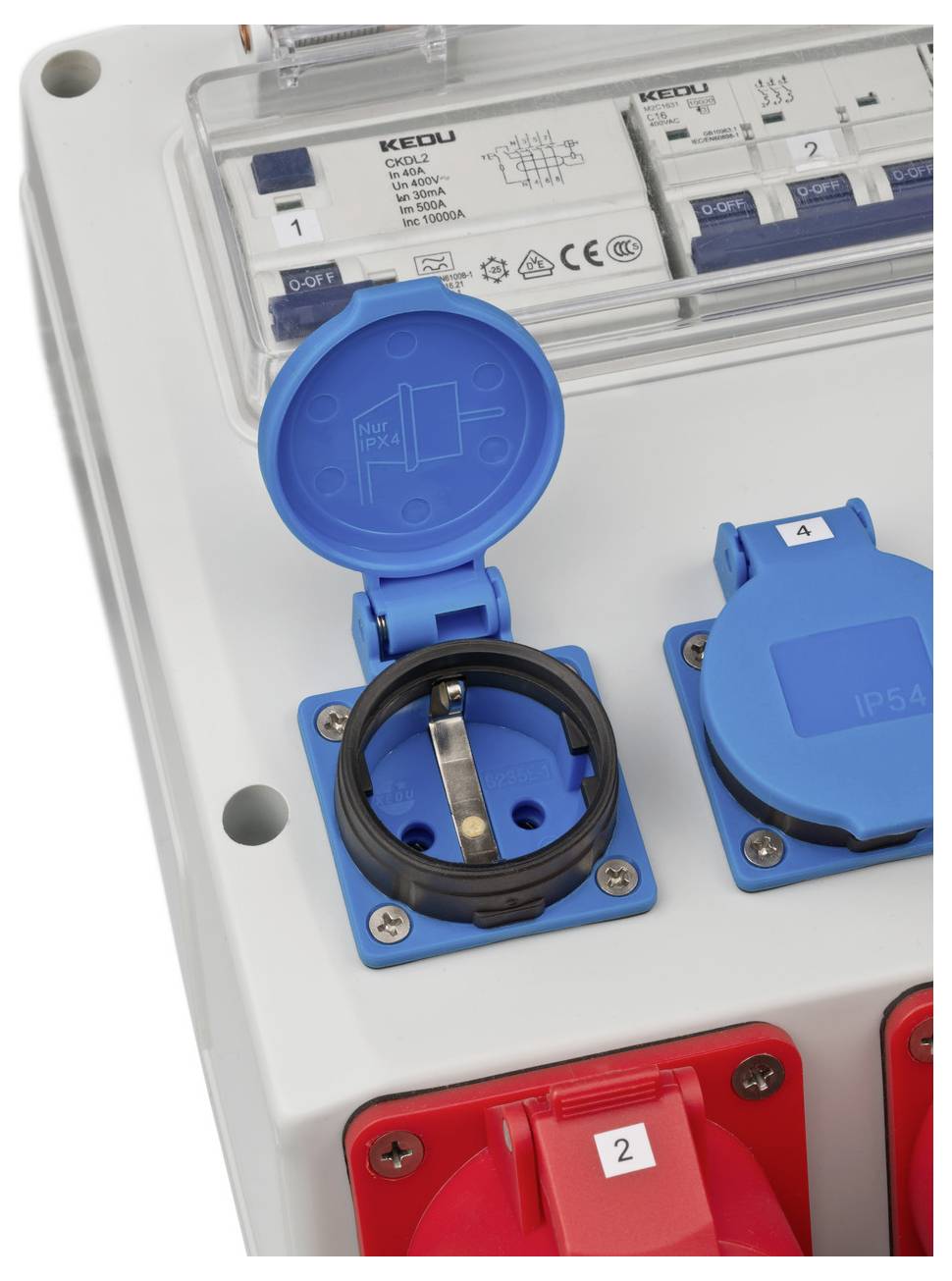 Pannello di controllo elettrico con prese di alimentazione industriali blu e rosse e interruttori automatici dietro un coperchio trasparente.