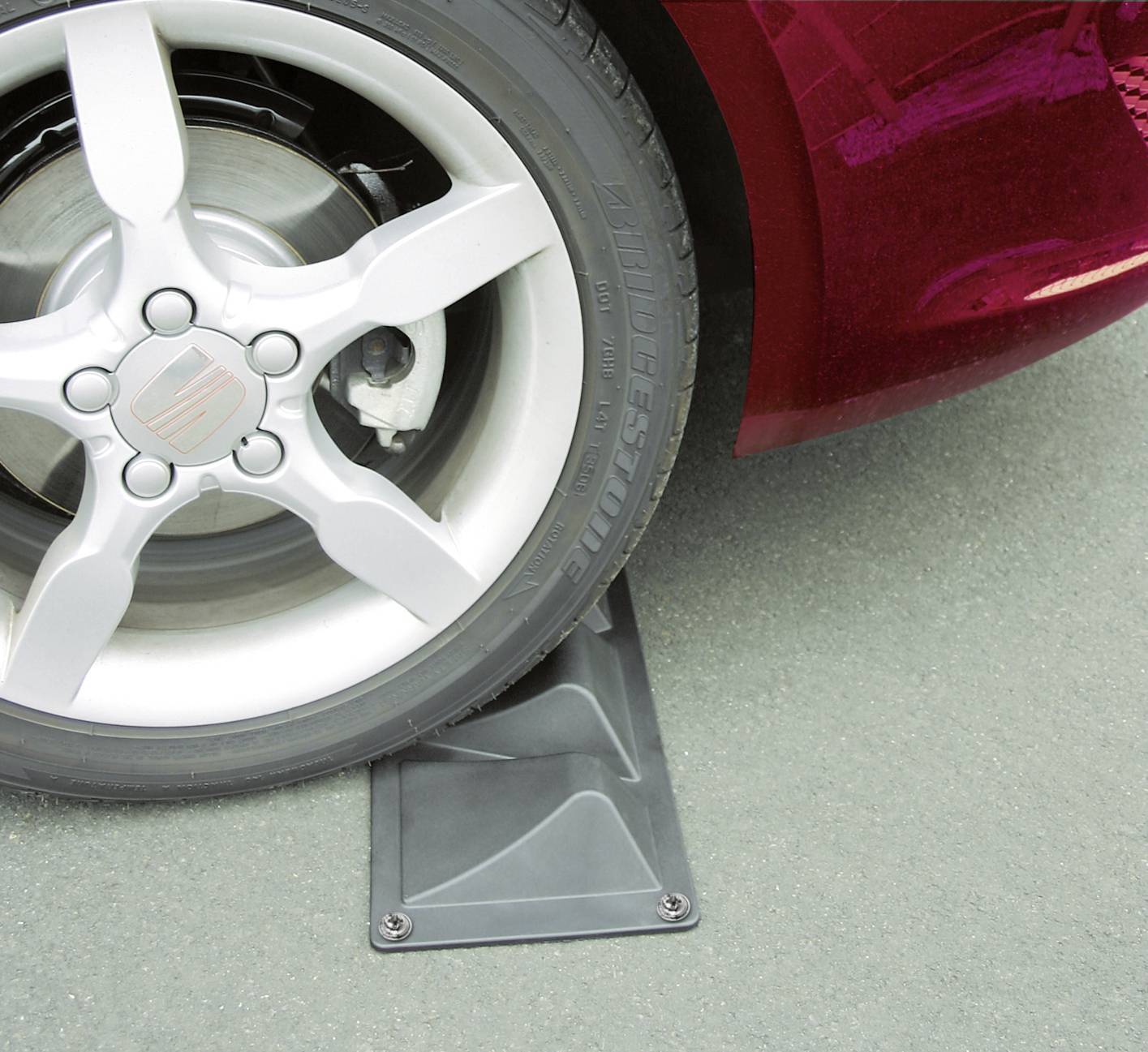 Auto rosso sull'asfalto con la ruota anteriore su una piattaforma grigia. Messa a fuoco sul pneumatico e sul lato del veicolo. Nessun dettaglio di sfondo riconoscibile.