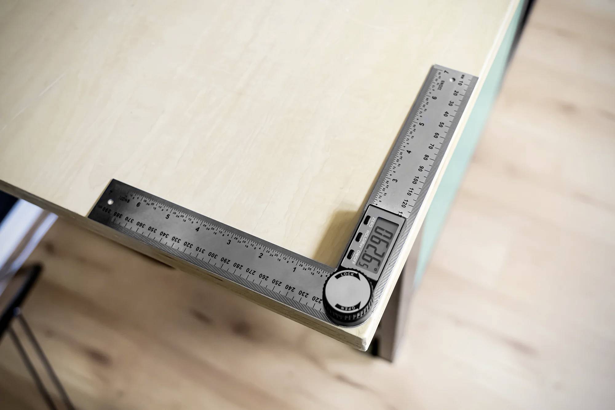 Un goniometro digitale misura l'angolo retto su un piano del tavolo, indicando 90 gradi.