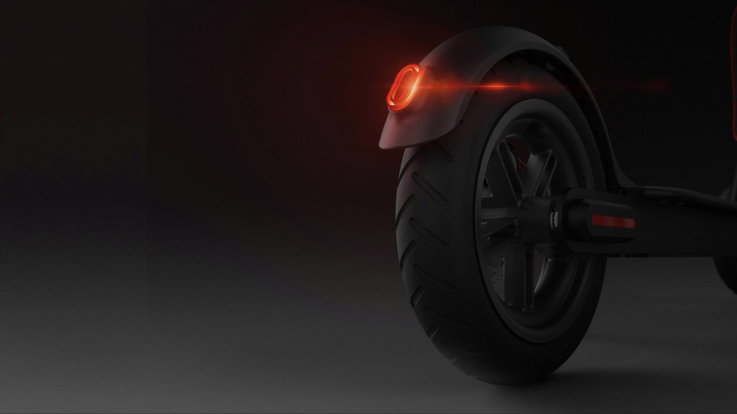 Ruota posteriore di uno scooter con una luce rossa posteriore illuminata in un ambiente buio, simboleggia sicurezza e visibilità al buio.