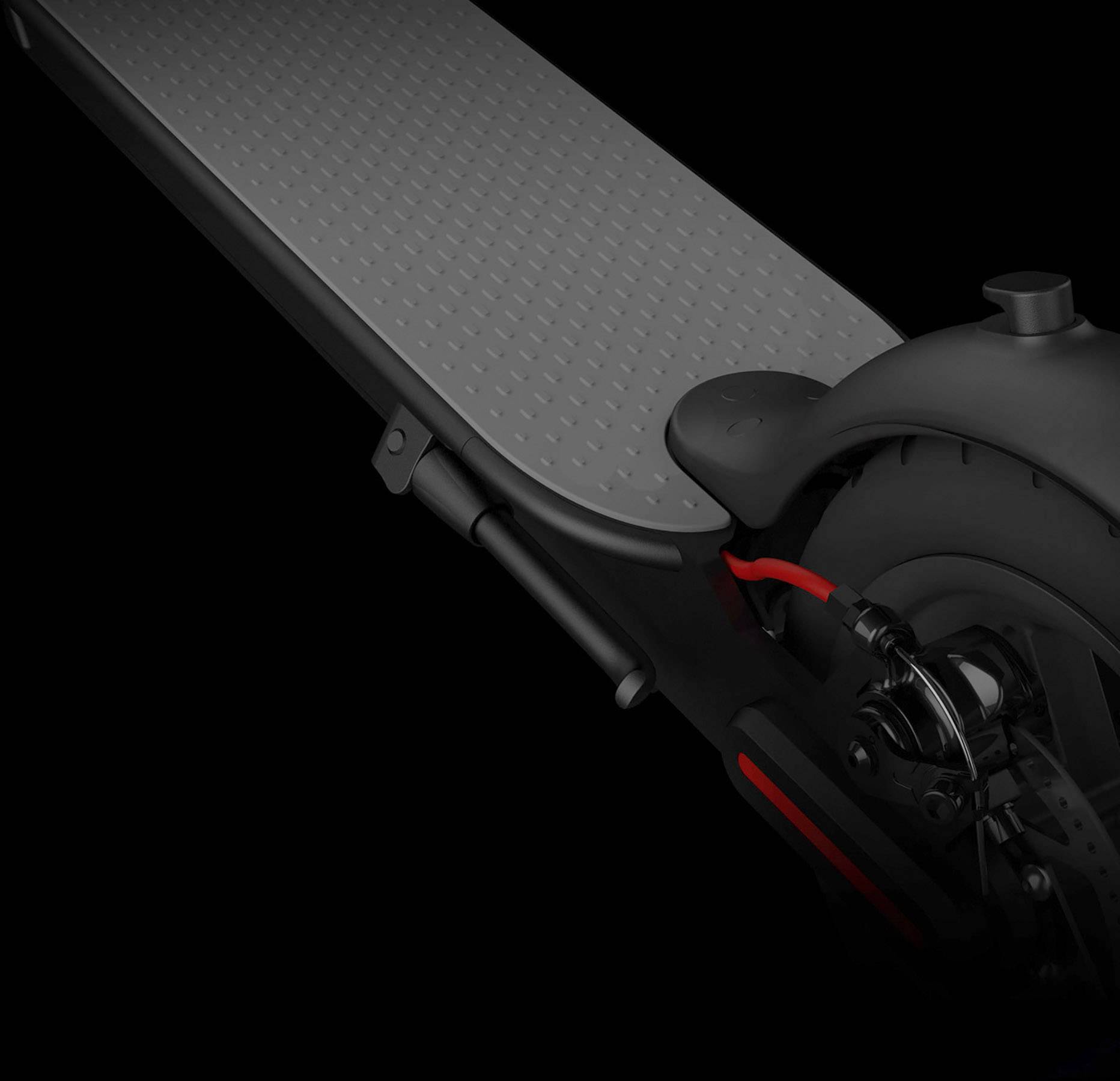 Primo piano di un monopattino con pedana nera e una striscia rossa di accento sulla ruota. Vista del posteriore e del meccanismo dei freni.