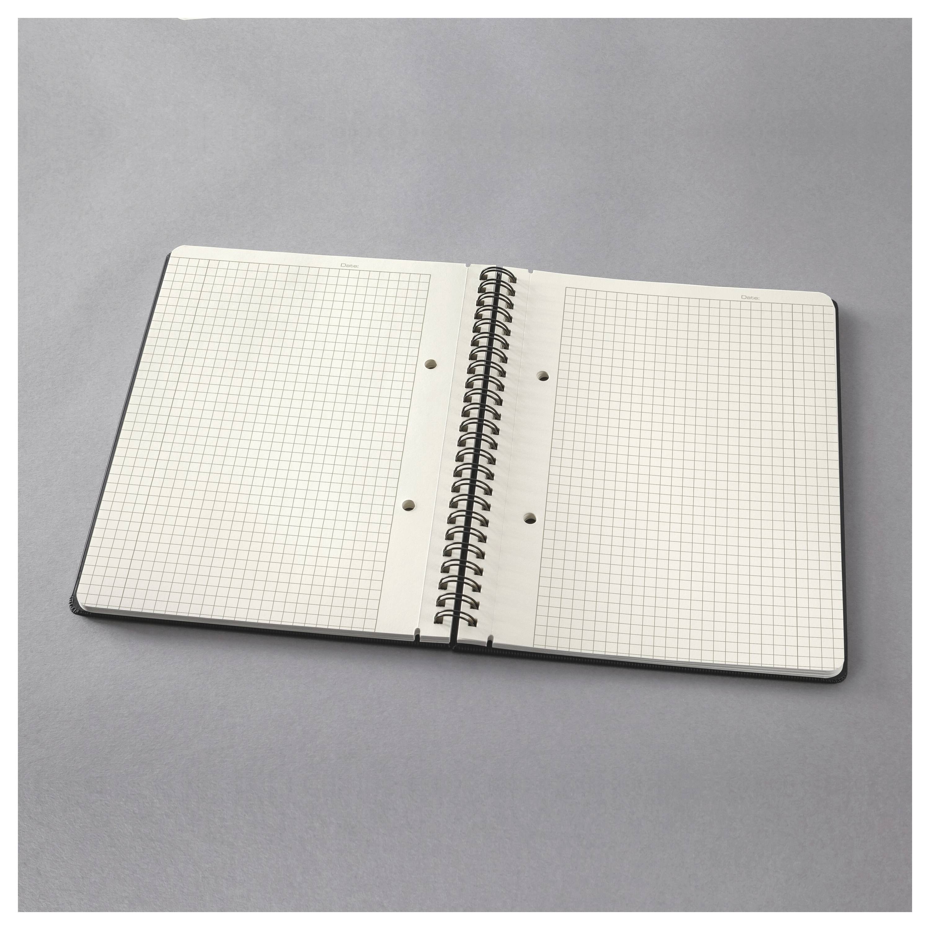 Quaderno a spirale aperto con pagine a quadretti su una superficie grigia.