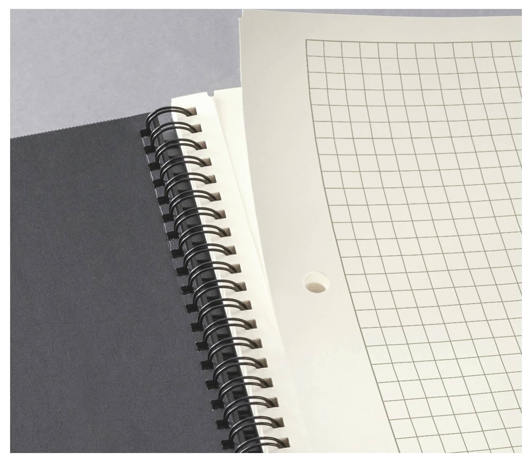 Primo piano di un quaderno a spirale con una pagina di carta millimetrata vuota sopra una copertina scura.
